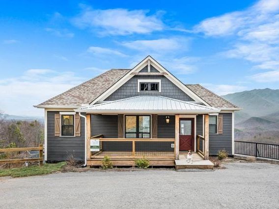 A cabin balcony with a private hot tub and rocking chairs facing panoramic mountain views. Guests can soak in the bubbling spa while enjoying breathtaking Smoky Mountain sunsets.