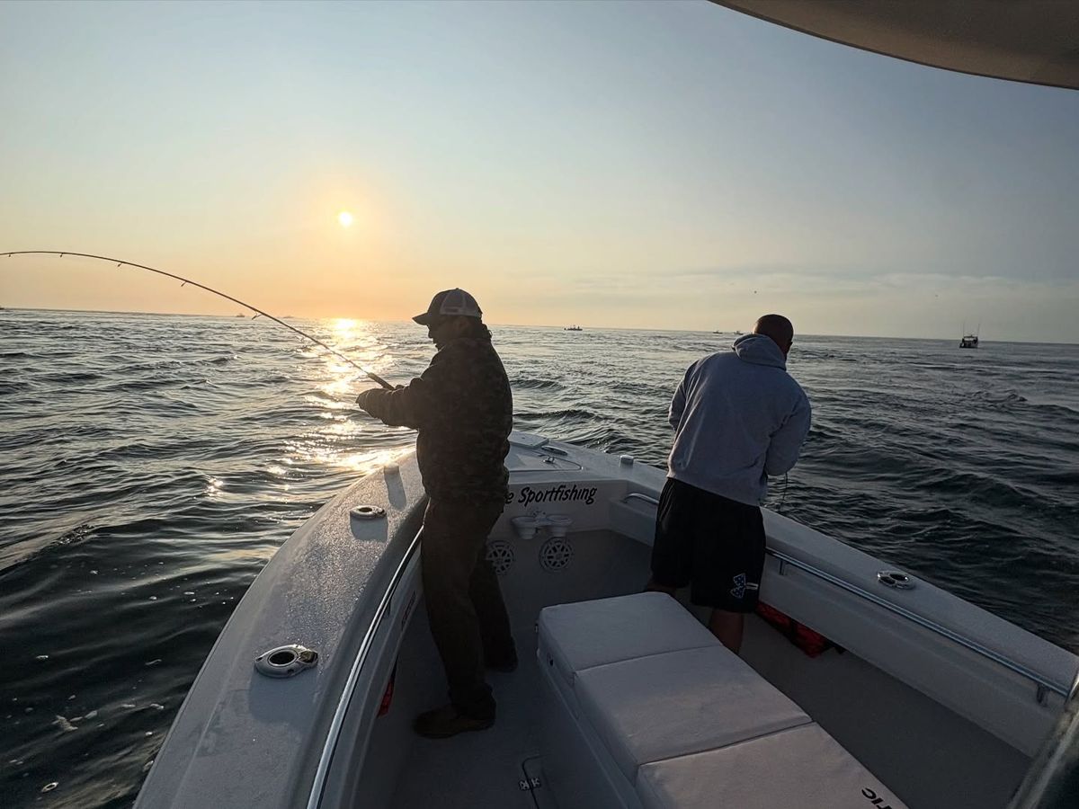 Two anglers fish from a sportfishing boat as the sun rises over the open Atlantic near Cape Cod. The calm water and golden light create the perfect setting for an early morning fishing trip. Sportfishing charters like On Fire Sportfishing are popular for catching striped bass and other local fish.