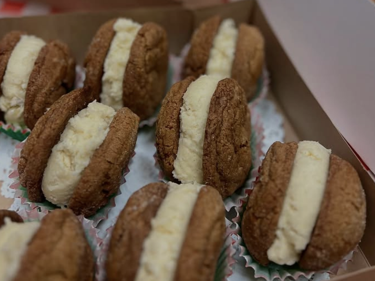 A box of cookie sandwiches with soft brown cookies and a thick layer of creamy white filling, each placed in a festive paper cup.