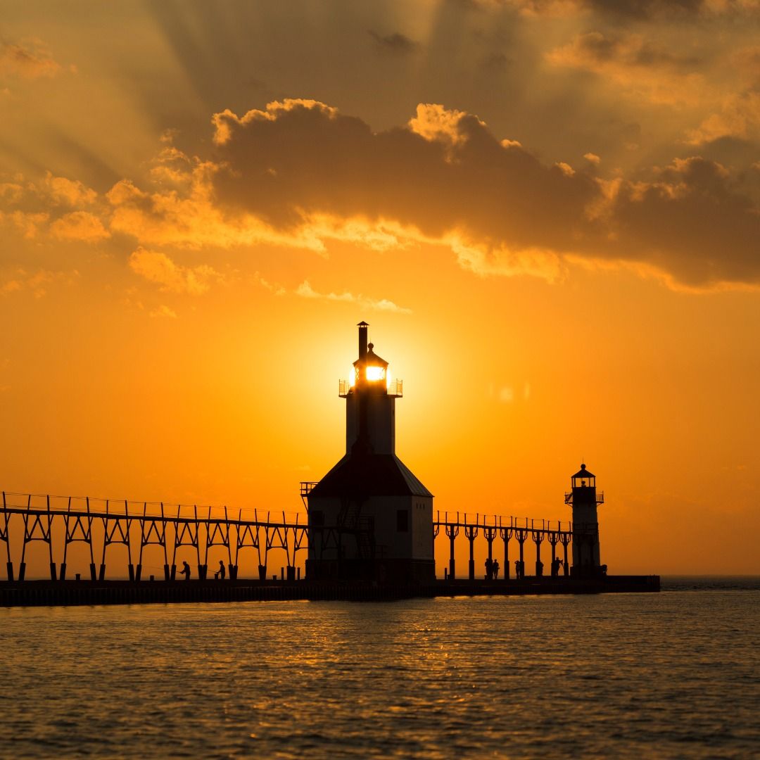 The iconic St. Joseph’s Lighthouse stands at the edge of Lake Michigan, glowing against a brilliant orange sunset. The calm water reflects the light, capturing the quiet beauty of this beloved lakeside landmark.