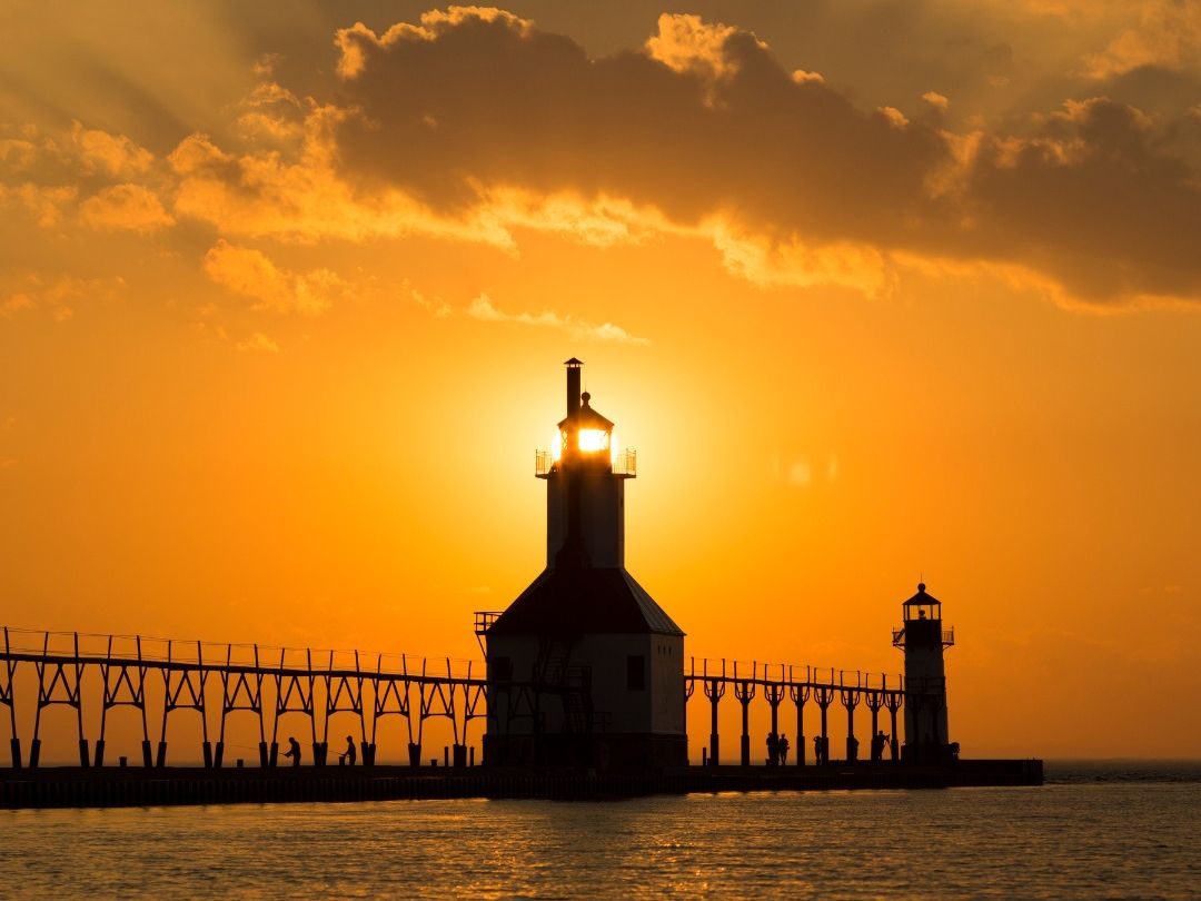 The iconic St. Joseph’s Lighthouse stands at the edge of Lake Michigan, glowing against a brilliant orange sunset. The calm water reflects the light, capturing the quiet beauty of this beloved lakeside landmark.