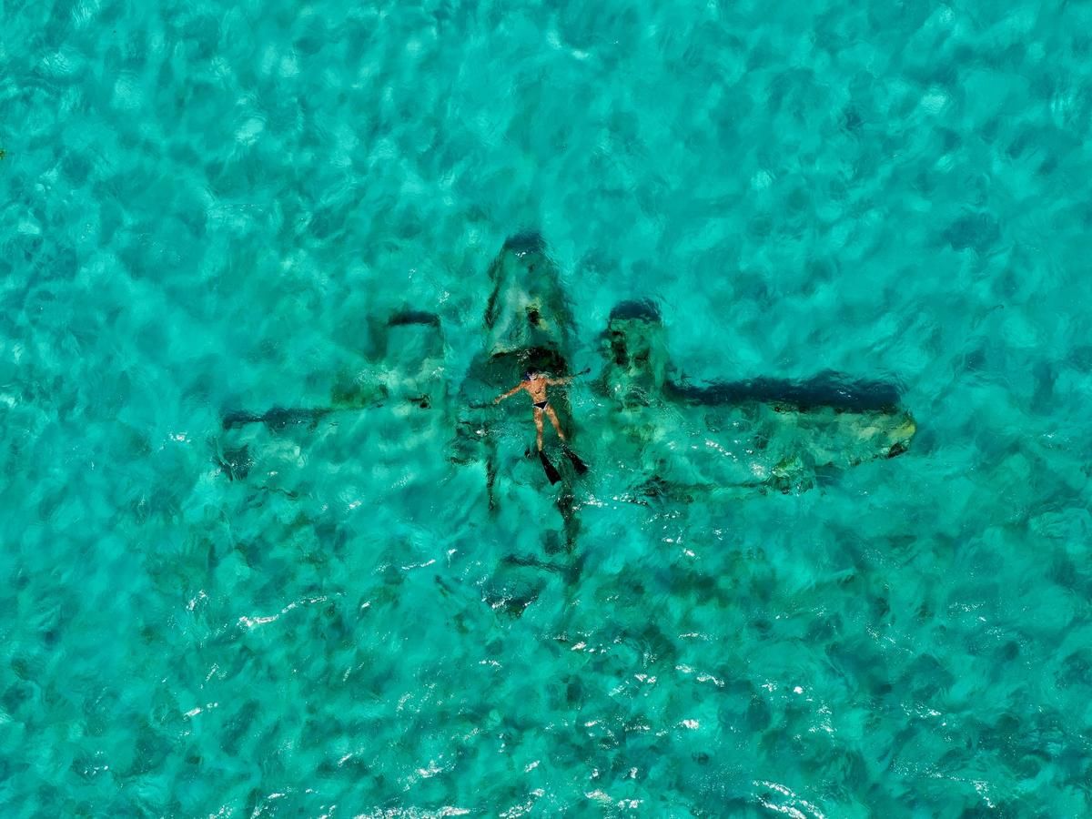 A snorkeler floats above a sunken plane wreck in crystal-clear turquoise waters in the Bahamas. This unique underwater adventure is perfect for explorers seeking both history and beauty beneath the sea.