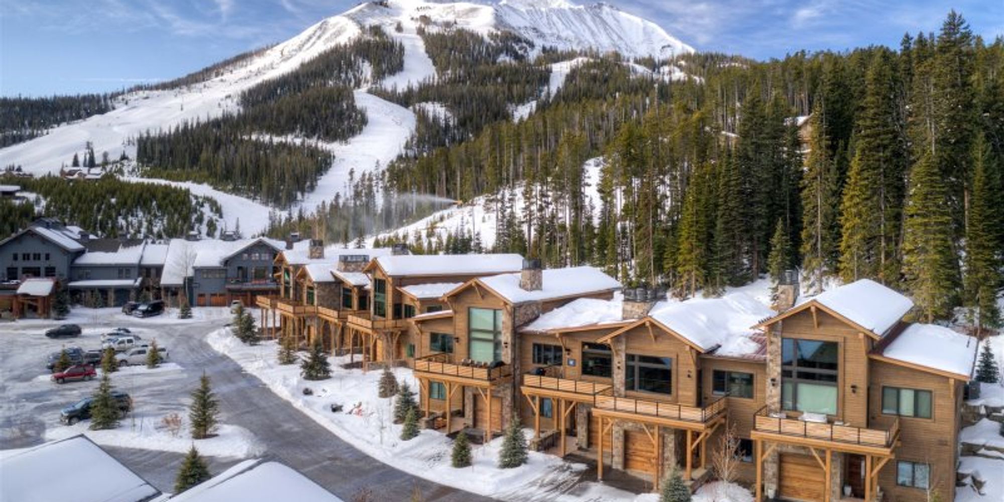 Snow-covered slopes tower over luxury mountain lodges at Big Sky, Montana. The cozy cabins with wood and stone finishes offer guests direct ski-in, ski-out access and stunning alpine views.
