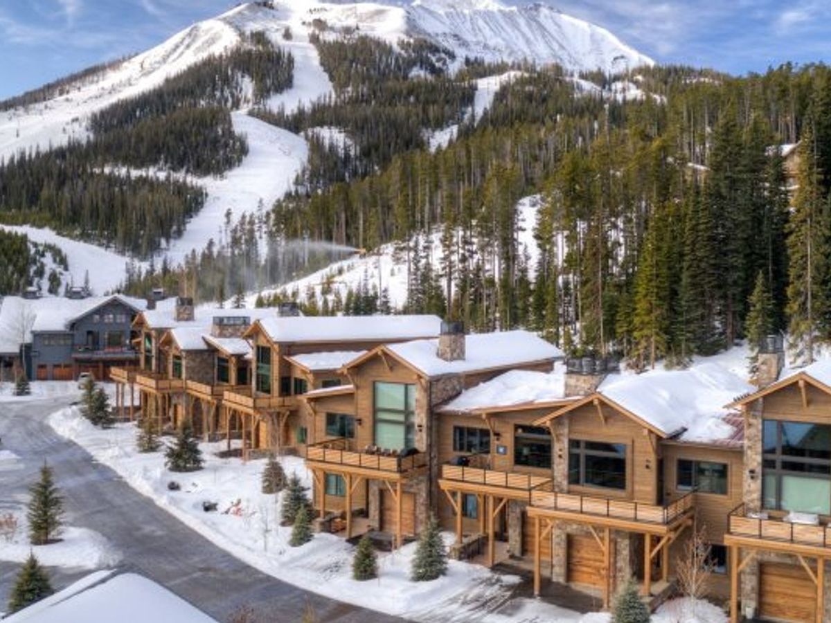 Snow-covered slopes tower over luxury mountain lodges at Big Sky, Montana. The cozy cabins with wood and stone finishes offer guests direct ski-in, ski-out access and stunning alpine views.