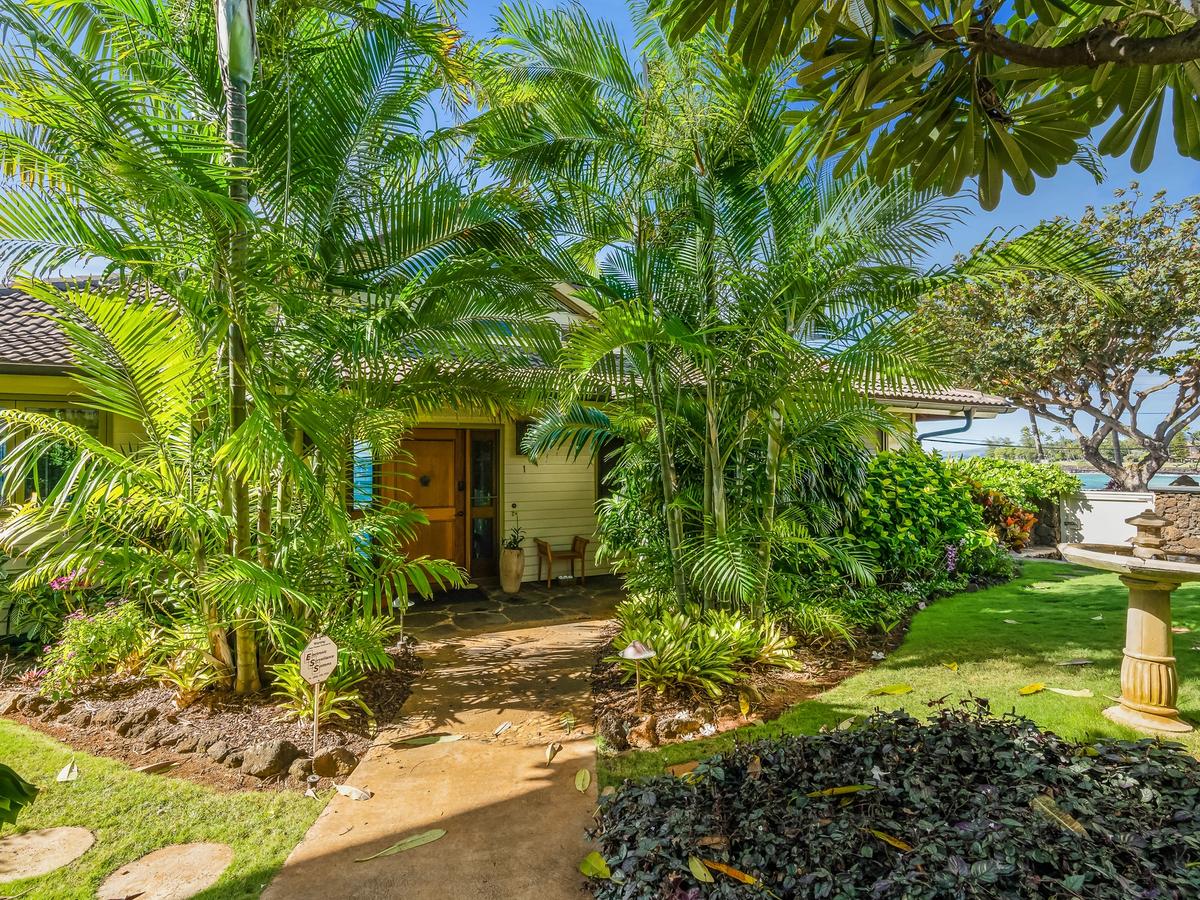 Tropical trees surrounding entrance to home with water fountain in the front yard