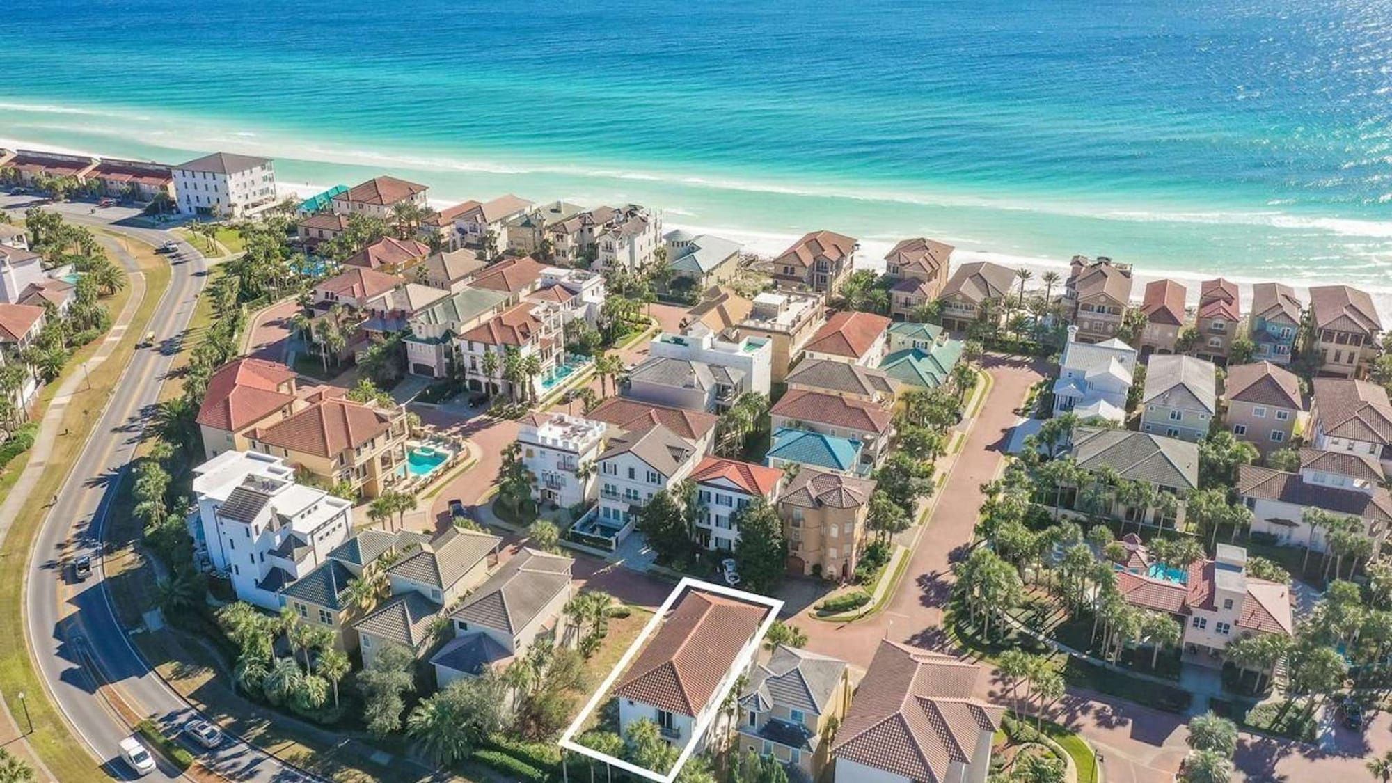 This aerial view highlights a beautiful beachside neighborhood with luxury homes just steps from the emerald waters of the Gulf. The marked property features classic architecture, a red-tiled roof, and easy access to scenic coastal roads and sugar-white sand.