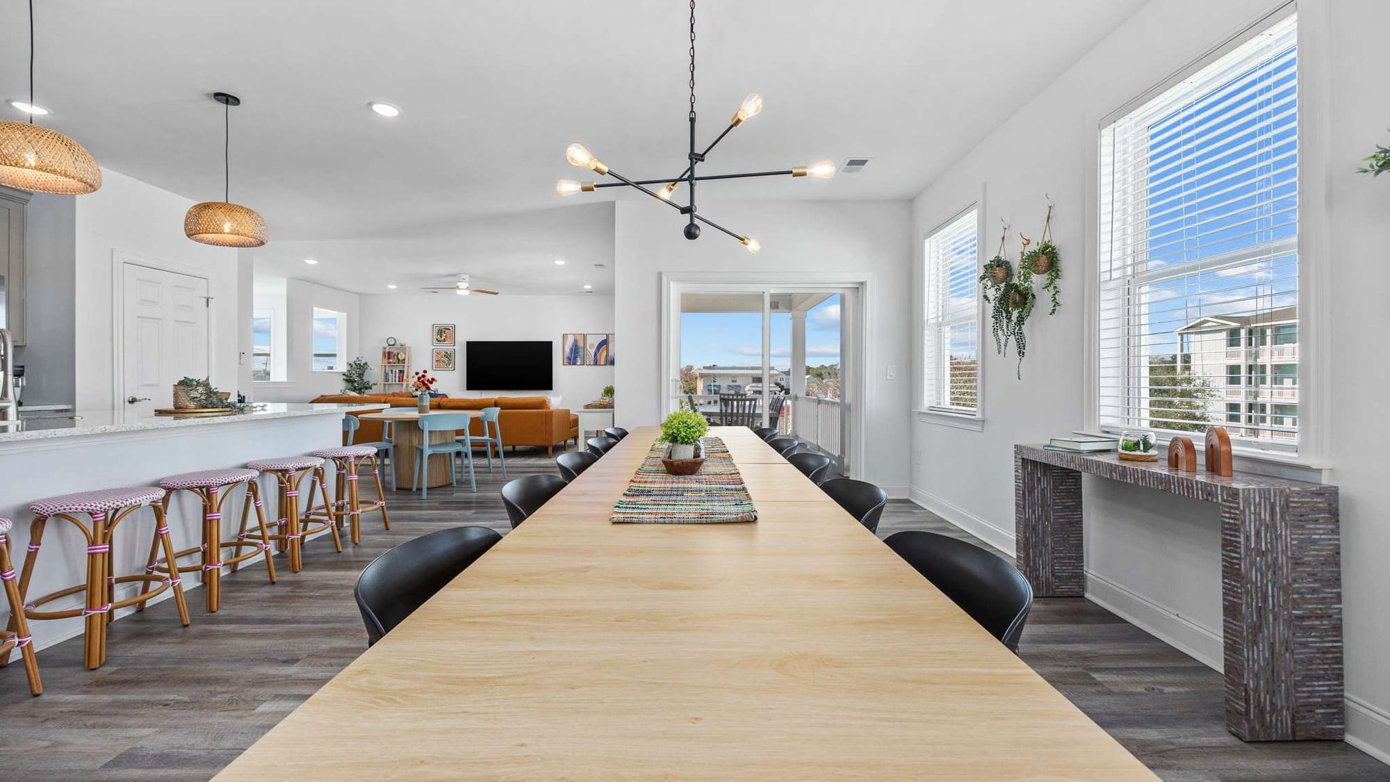 Spacious dining area with a long wooden table offers plenty of seating for group meals and celebrations. The open layout connects the kitchen and living room, making it easy to host large family dinners.