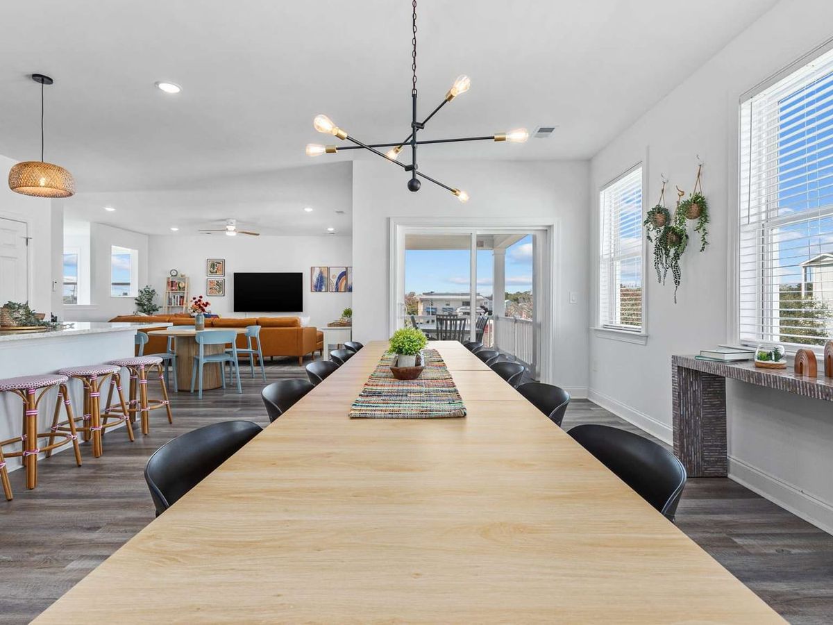 Spacious dining area with a long wooden table offers plenty of seating for group meals and celebrations. The open layout connects the kitchen and living room, making it easy to host large family dinners.