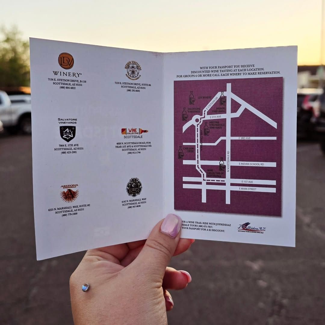 A hand holds up a wine passport showing a map of local wineries in Scottsdale. The soft sunset light adds warmth to this guide for an afternoon of tasting and exploration.