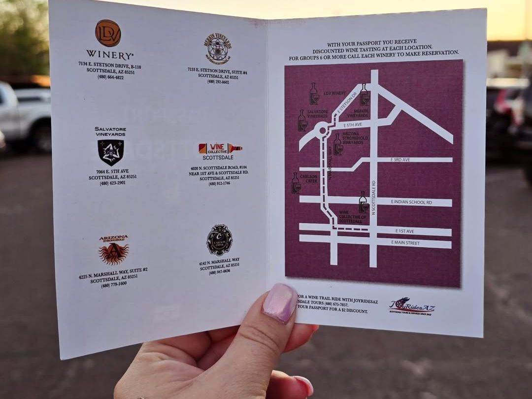 A hand holds up a wine passport showing a map of local wineries in Scottsdale. The soft sunset light adds warmth to this guide for an afternoon of tasting and exploration.