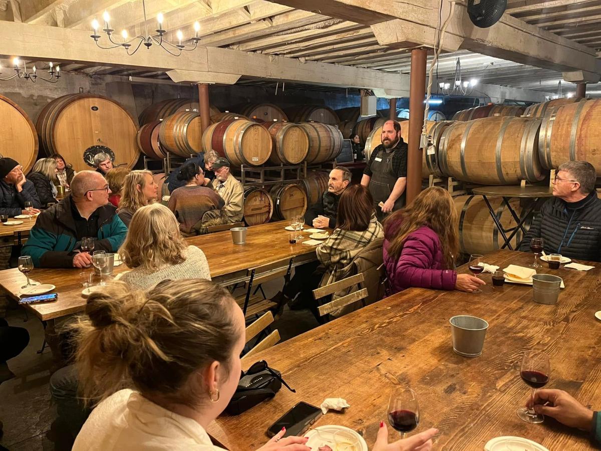 Guests enjoy a guided wine tasting inside the Ravines Wine Cellars barrel room, surrounded by oak barrels. The setting feels warm and intimate, perfect for learning about Finger Lakes wines.