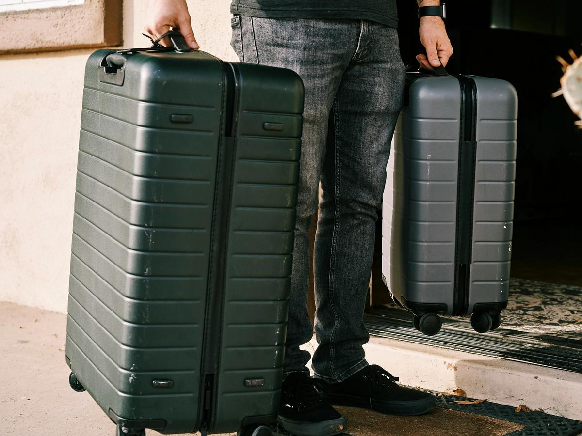 A person stands in a doorway holding two modern hard-shell suitcases