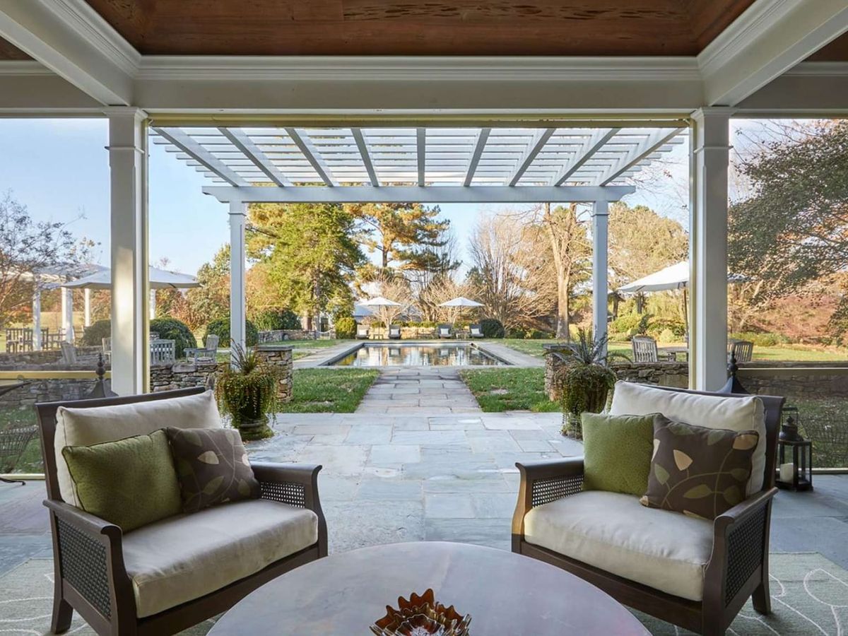 A covered outdoor patio with wicker chairs and a dining table overlooks a private pool and mountain views. Surrounded by nature and open space, this farmhouse setting is ideal for gatherings and peaceful mornings.