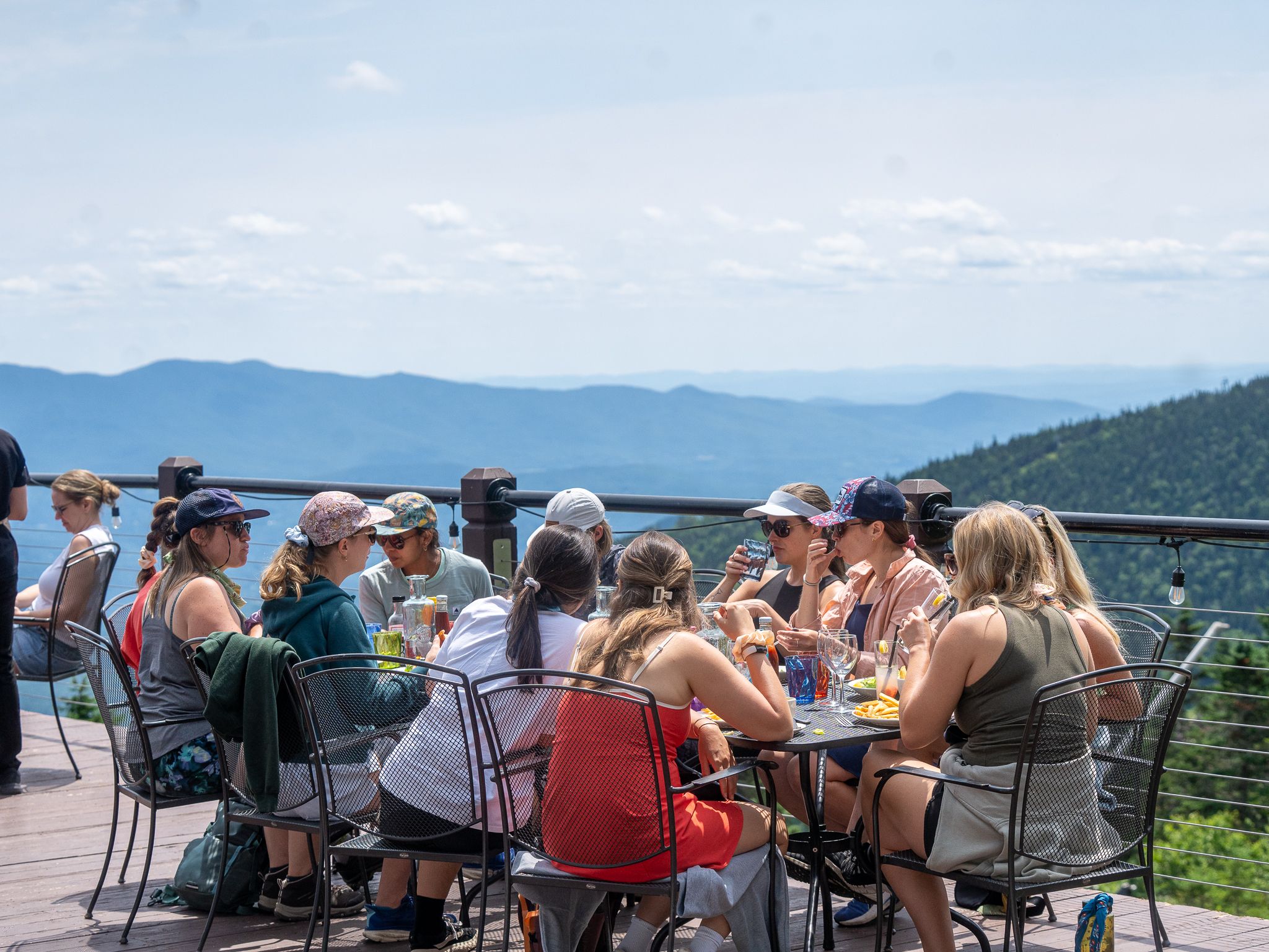 Guests enjoy lunch at an outdoor deck overlooking sweeping mountain views at Stowe Mountain Resort. This scenic spot is popular for casual dining, drinks, and soaking in the fresh alpine air.