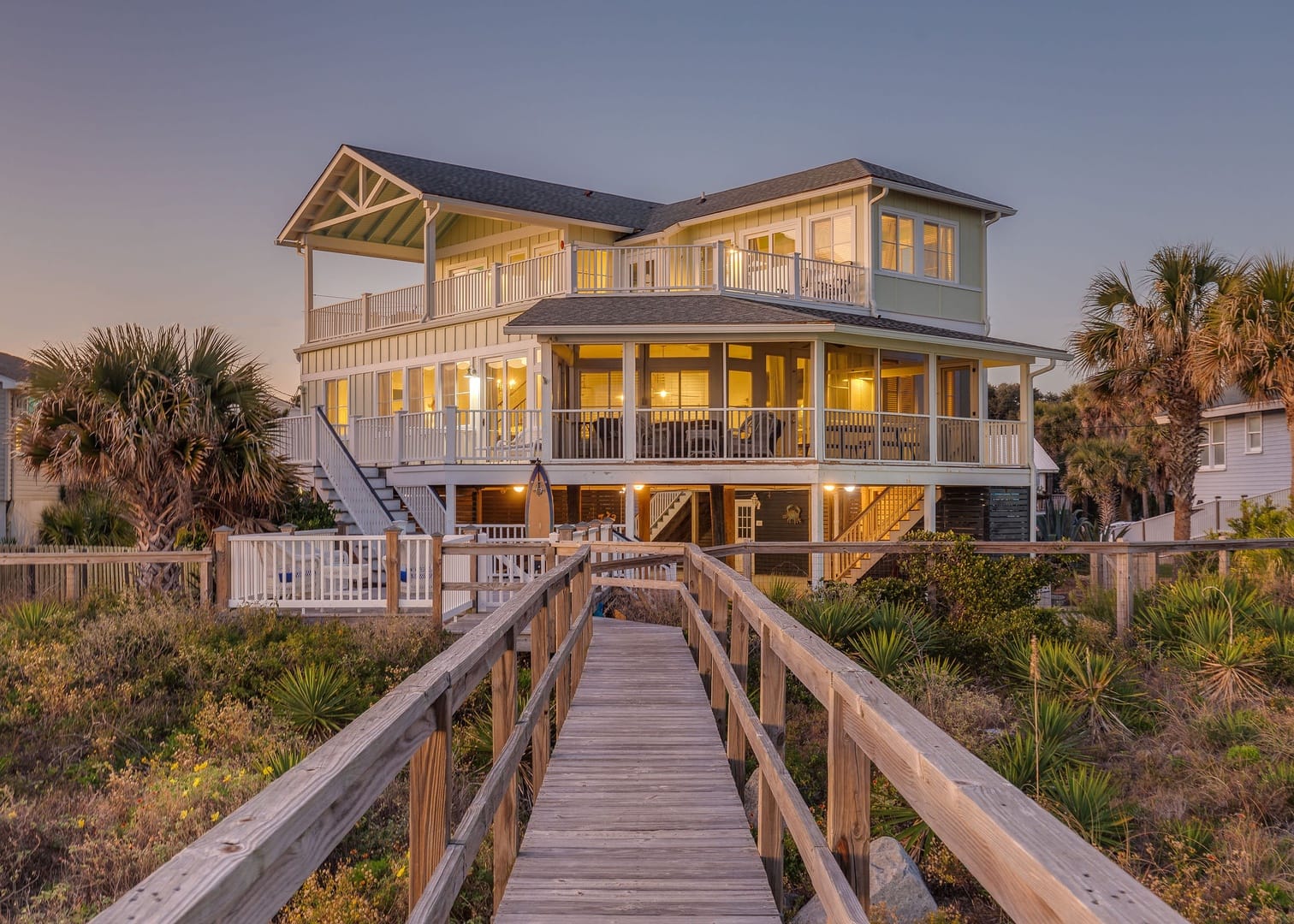Open dining and living area with a large wood table, coastal decor, and wide windows facing the ocean in Folly Beach. The bright layout makes it easy to enjoy meals, relax, and take in beach views without leaving the room.