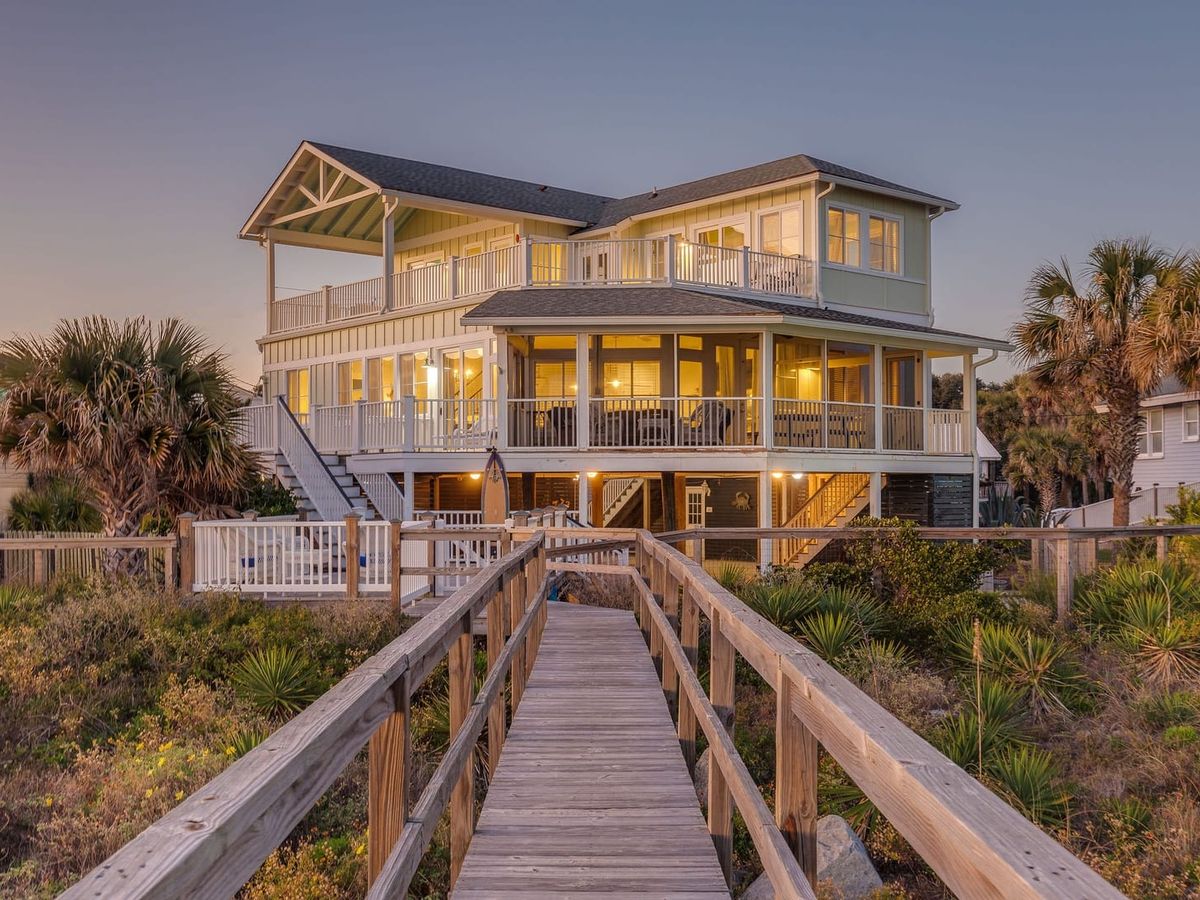 Open dining and living area with a large wood table, coastal decor, and wide windows facing the ocean in Folly Beach. The bright layout makes it easy to enjoy meals, relax, and take in beach views without leaving the room.