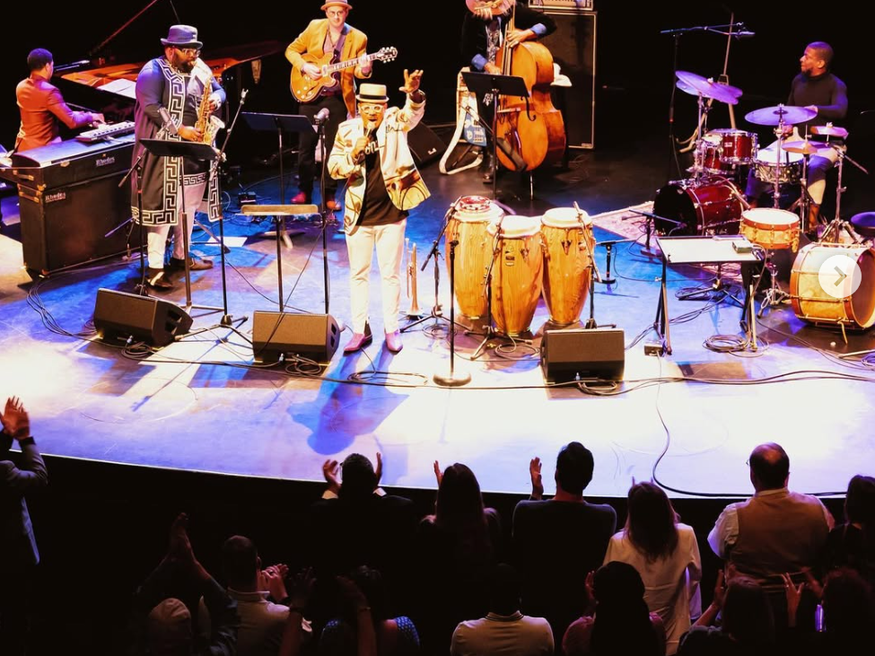 Jazz band on stage with gear and people dancing in front of it clapping their hands