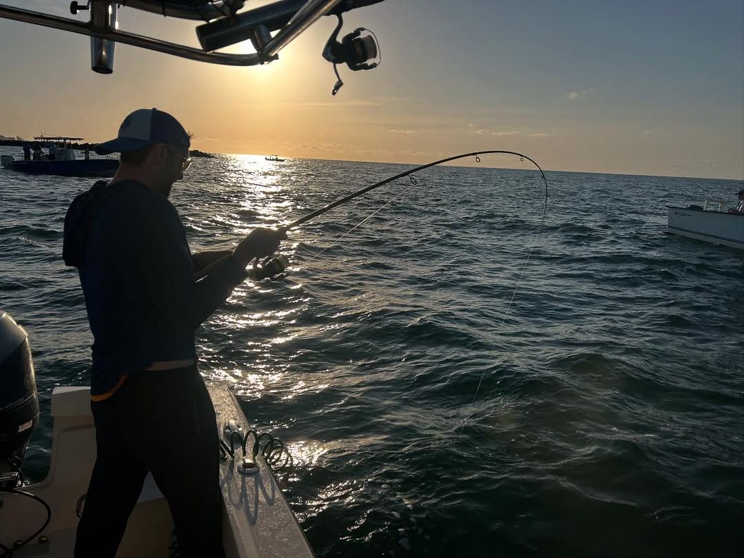 A man fights a strong catch while deep sea fishing with All Jack’d Up Charters in Perdido Key, as the sun sets over the Gulf waters.