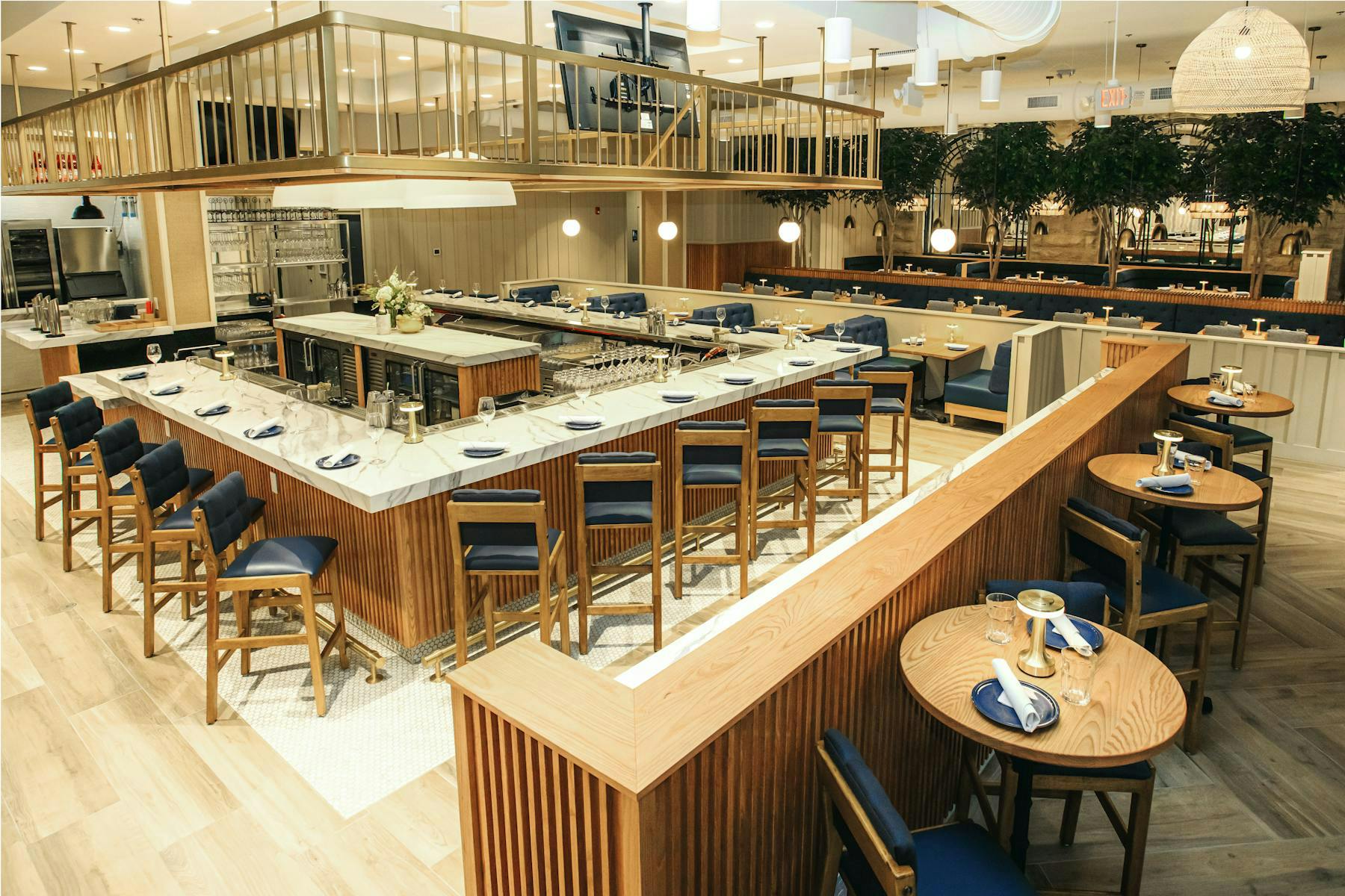 A chic modern restaurant with a marble-topped bar surrounded by wooden and navy blue seating. The open, inviting layout blends sophistication and comfort, ideal for gatherings and casual dining.