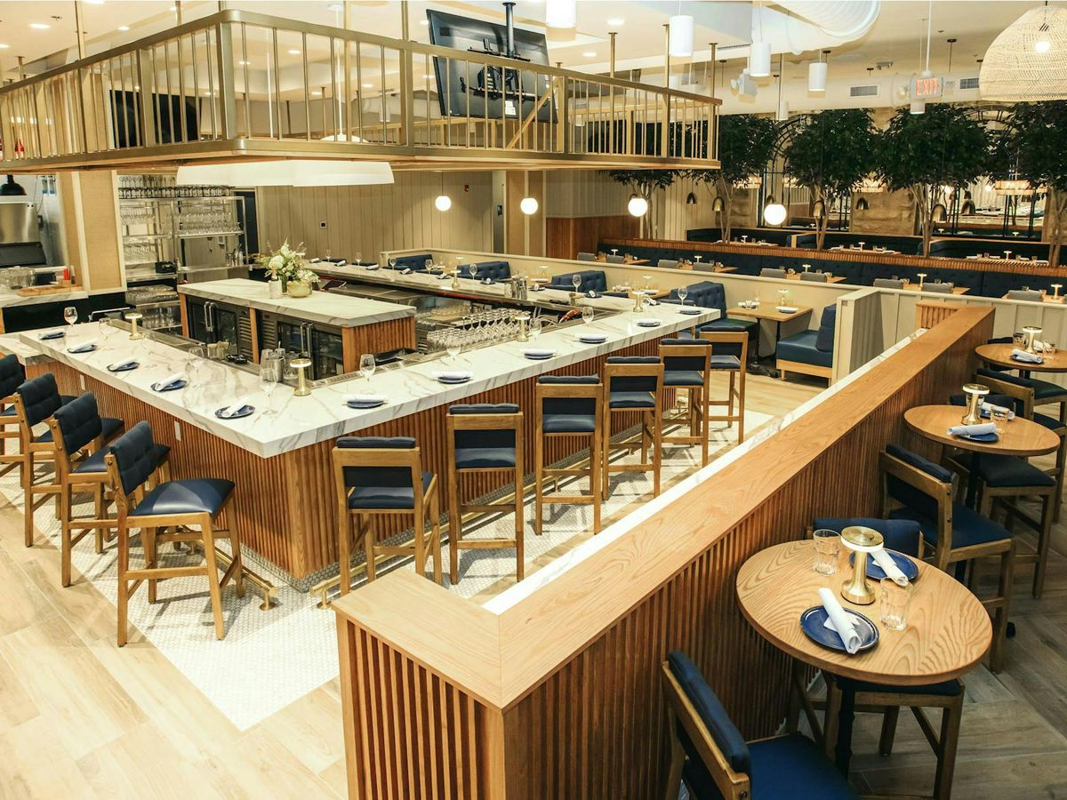 A chic modern restaurant with a marble-topped bar surrounded by wooden and navy blue seating. The open, inviting layout blends sophistication and comfort, ideal for gatherings and casual dining.