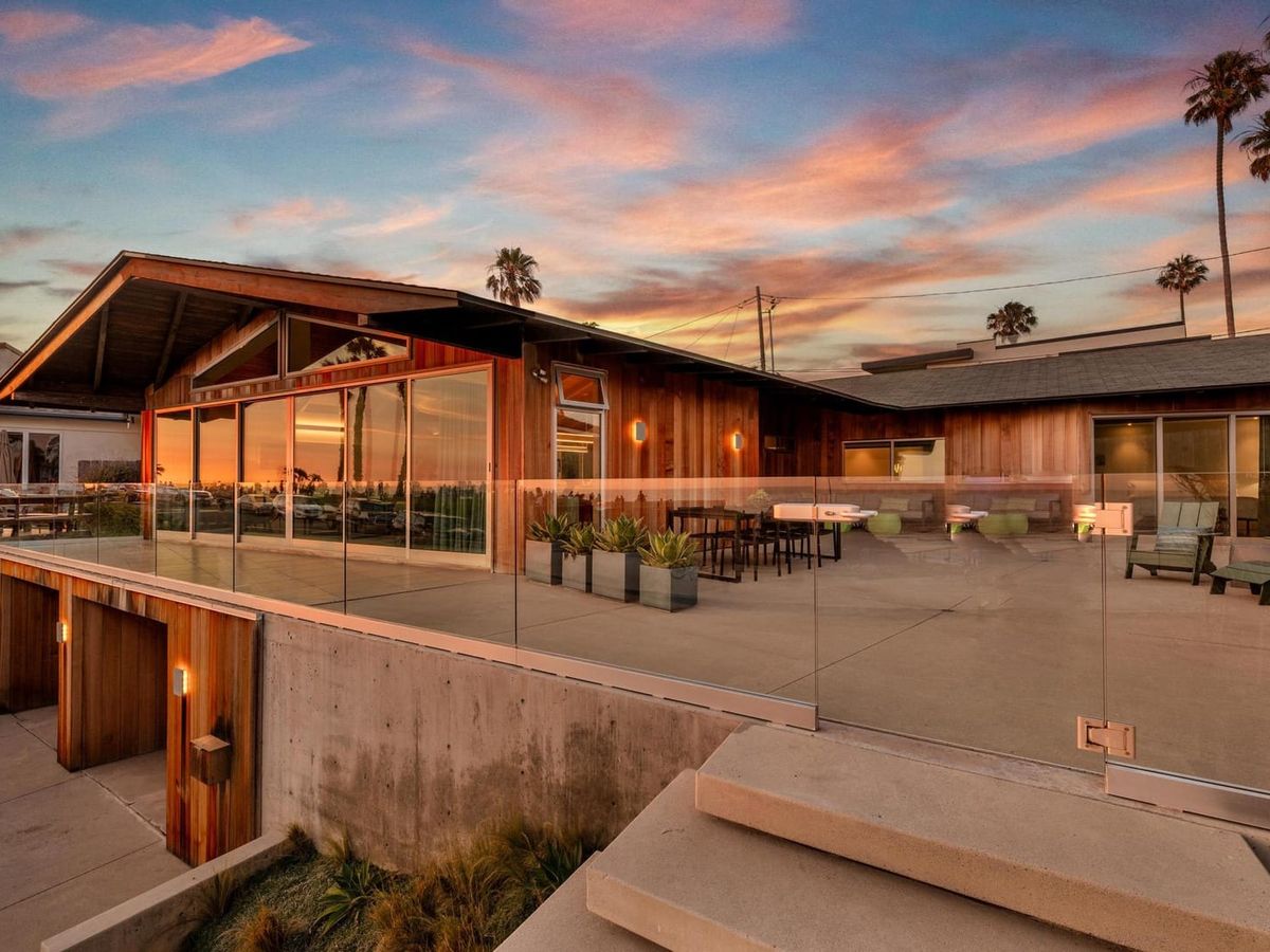 A modern coastal home in San Diego with glass walls and sleek wood details, overlooking a breathtaking sunset. The wide terrace and ocean backdrop make this a dream setting for evening gatherings.
