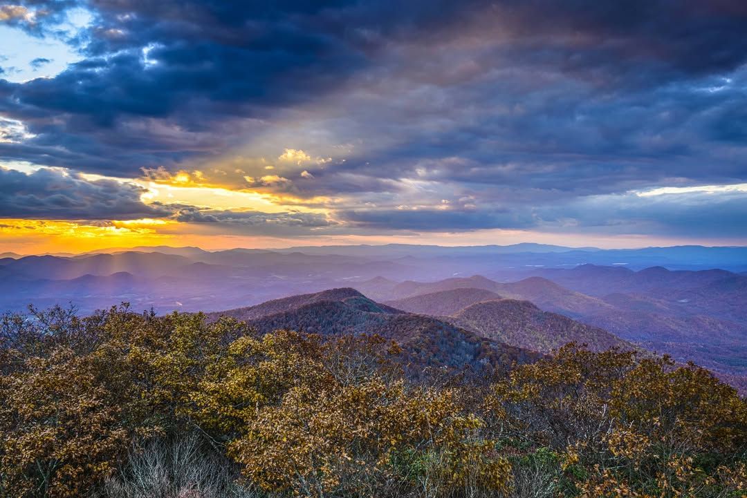 Golden sunset light breaks through the clouds over the rolling mountain ridges at Brasstown Bald, the highest point in Georgia. This scenic overlook offers wide views of the Blue Ridge Mountains, making it a popular spot for sunrise and sunset photos in the fall.