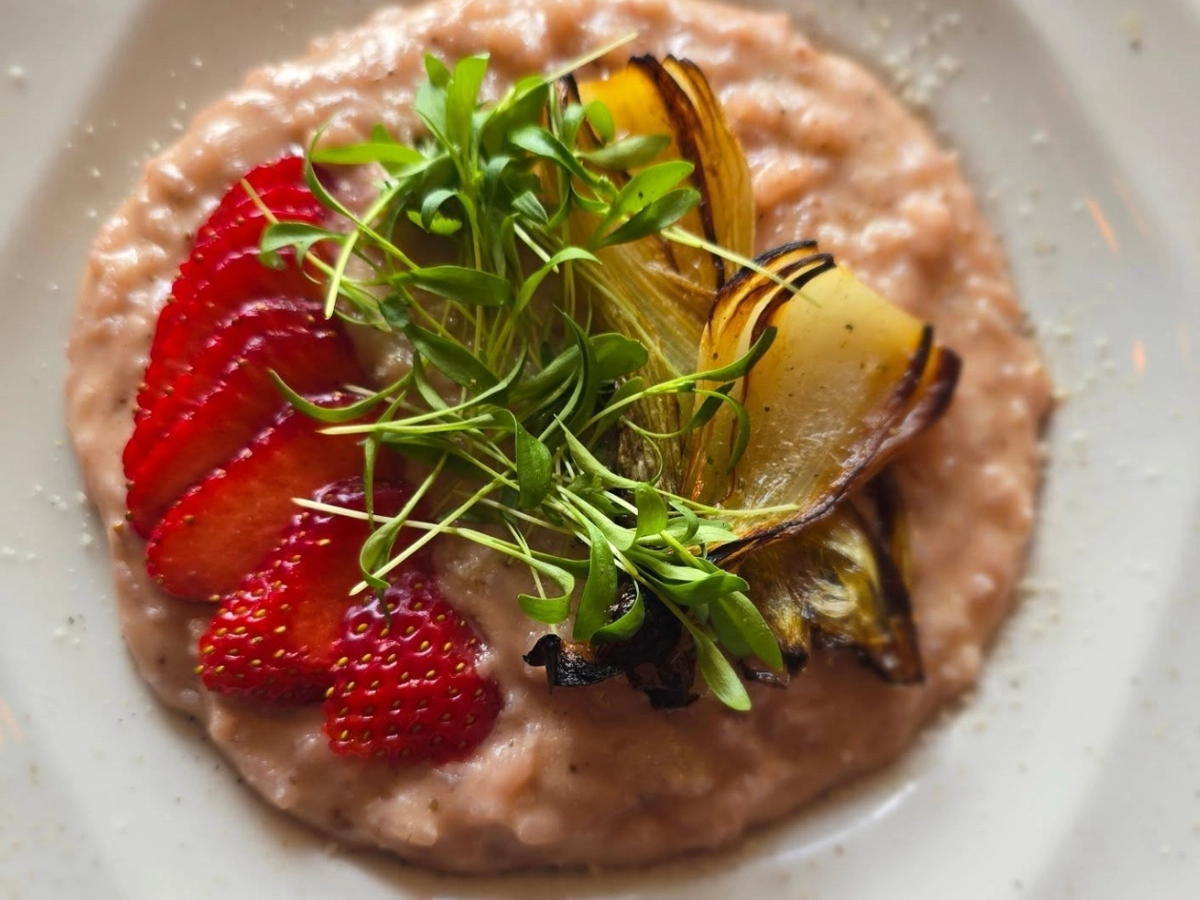 A gourmet plate of creamy pink risotto topped with sliced strawberries, charred endive, and fresh microgreens.
