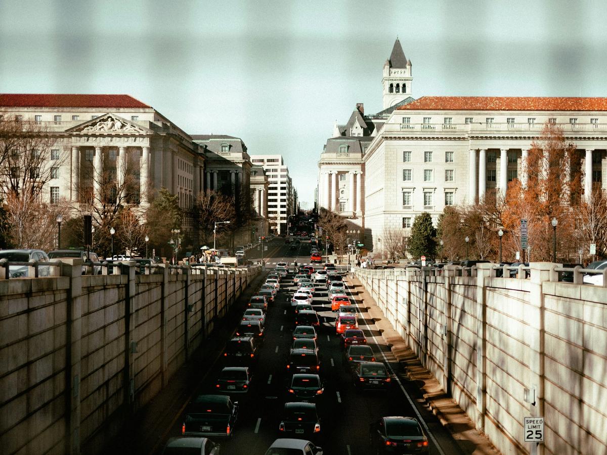 Downtown Washington, D.C. traffic jam in a sunken roadway, surrounded by neoclassical government buildings and framed by leafless winter trees.