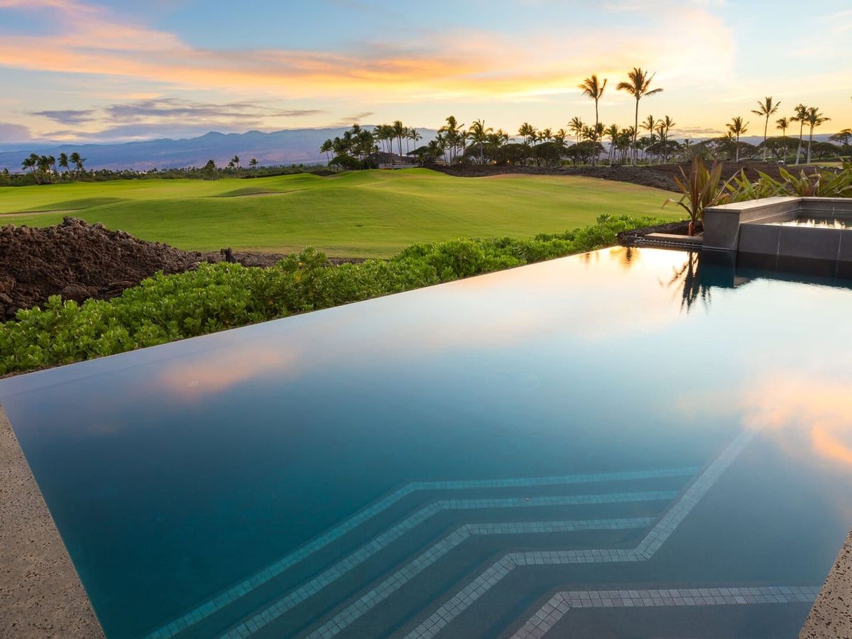 A luxury infinity pool overlooks a green golf course with palm trees and lava rocks at sunset. This high-end Hawaiian retreat blends comfort, nature, and stunning views in one peaceful spot