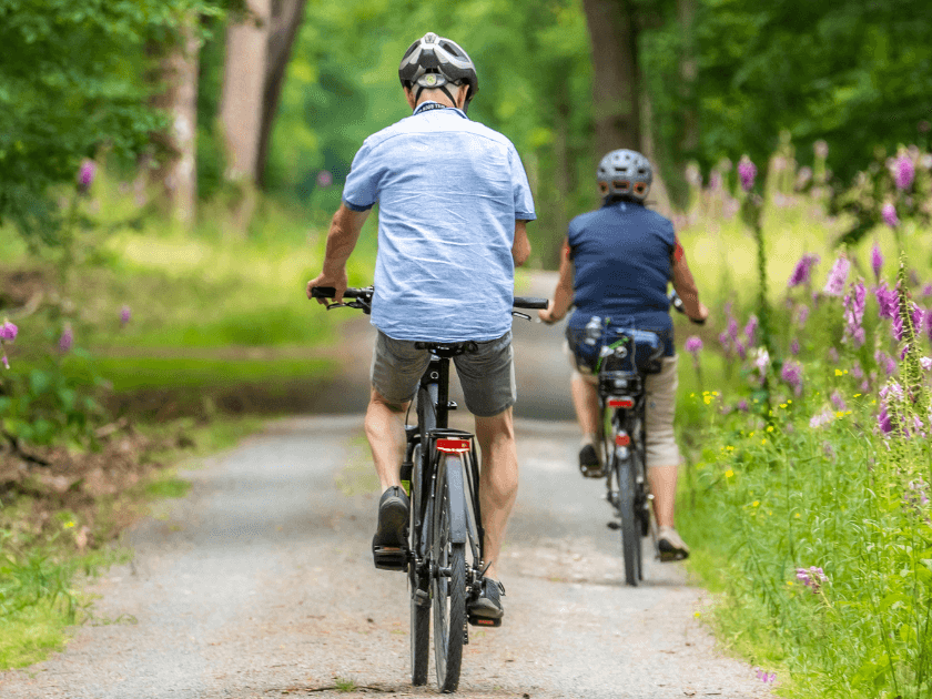 Two people ride bikes through a lush forest trail on Kiawah Island, surrounded by wildflowers and tall trees. This quiet, scenic path is perfect for nature lovers looking to explore the island beyond the beach.