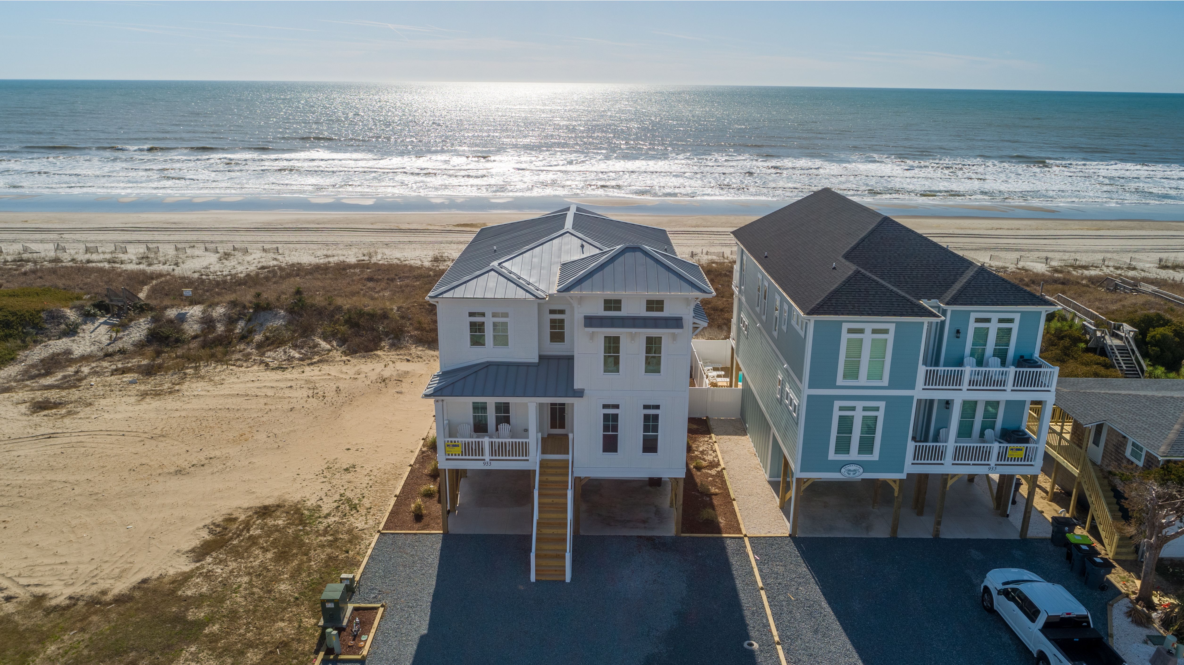 White house with wooden stairs leading up to fron door and beach surrounding it