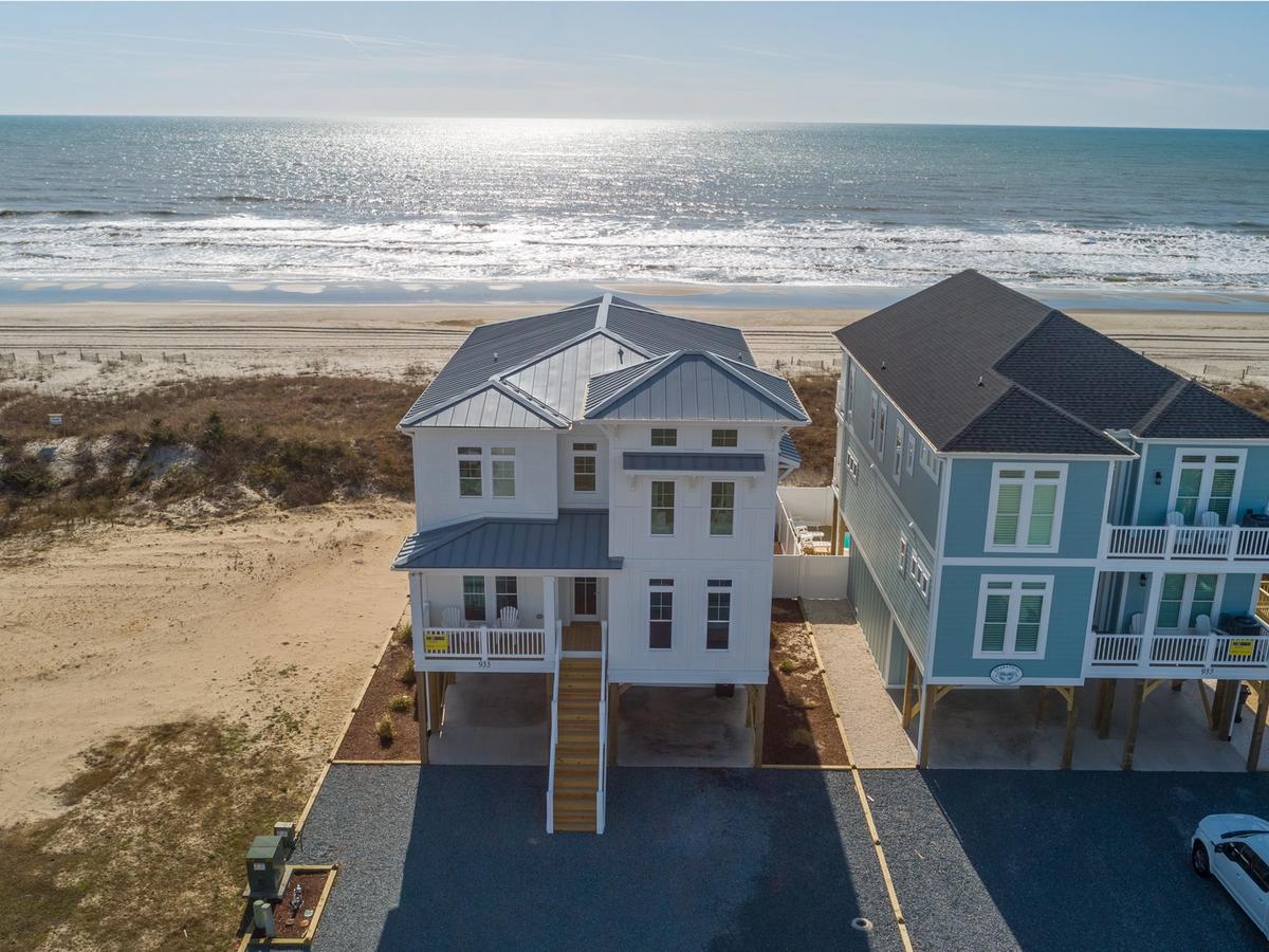 White house with wooden stairs leading up to fron door and beach surrounding it