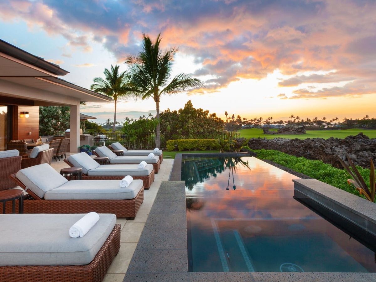 A row of cushioned loungers sits beside a sleek pool that reflects the warm colors of the sunset. The outdoor living space feels calm and open, giving you the perfect spot to unwind after a full day of exploring. It’s the kind of place where time slows down and every sunset feels special.
