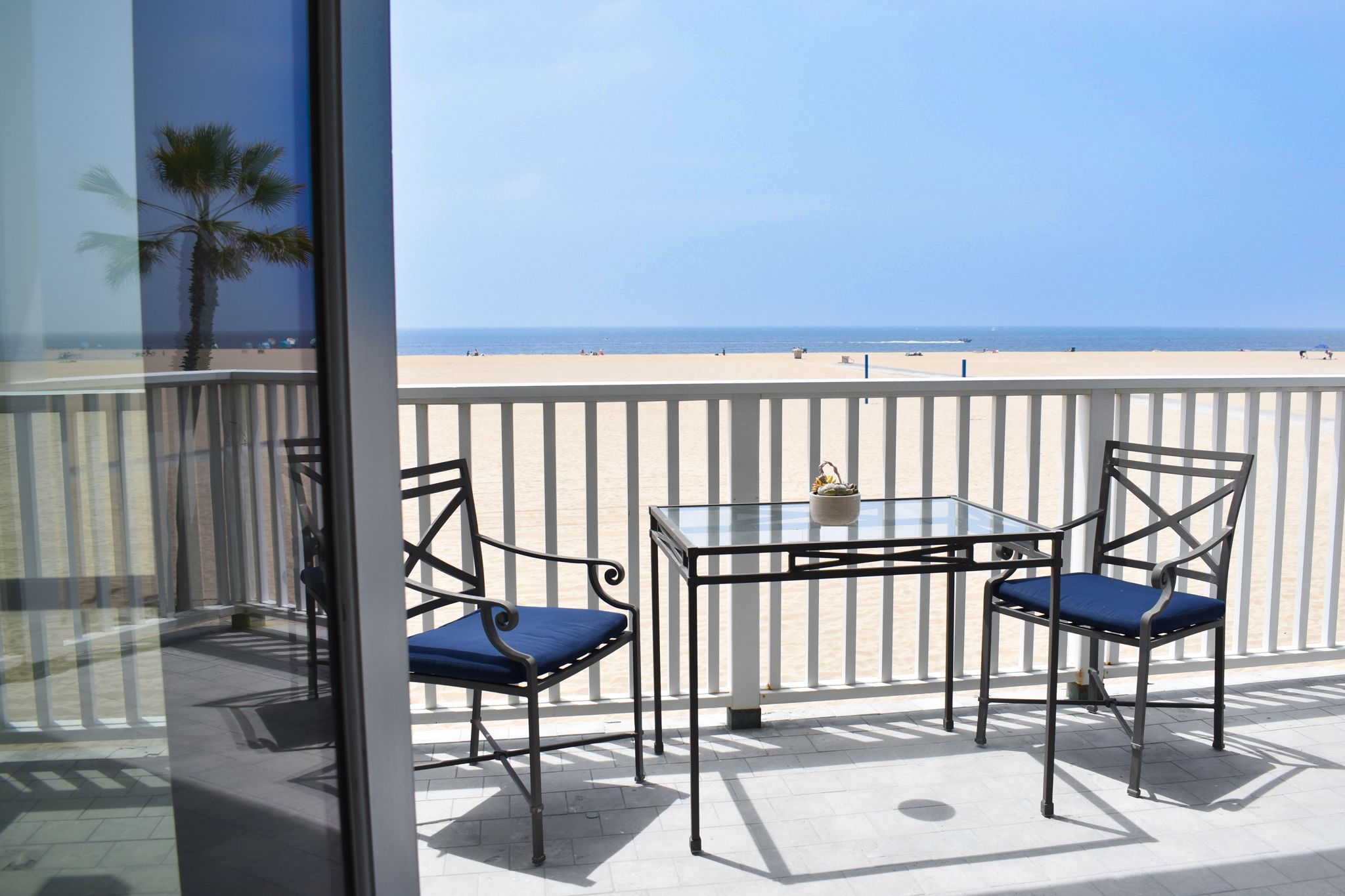Oceanfront balcony at a Newport Beach vacation rental with direct beach access, featuring a glass-top bistro table, two chairs, and panoramic views of the Pacific Ocean.