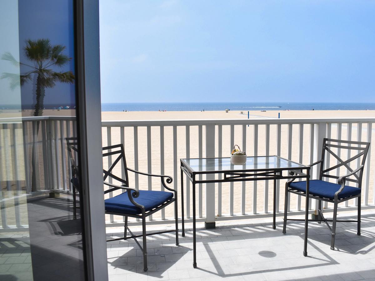 Oceanfront balcony at a Newport Beach vacation rental with direct beach access, featuring a glass-top bistro table, two chairs, and panoramic views of the Pacific Ocean.