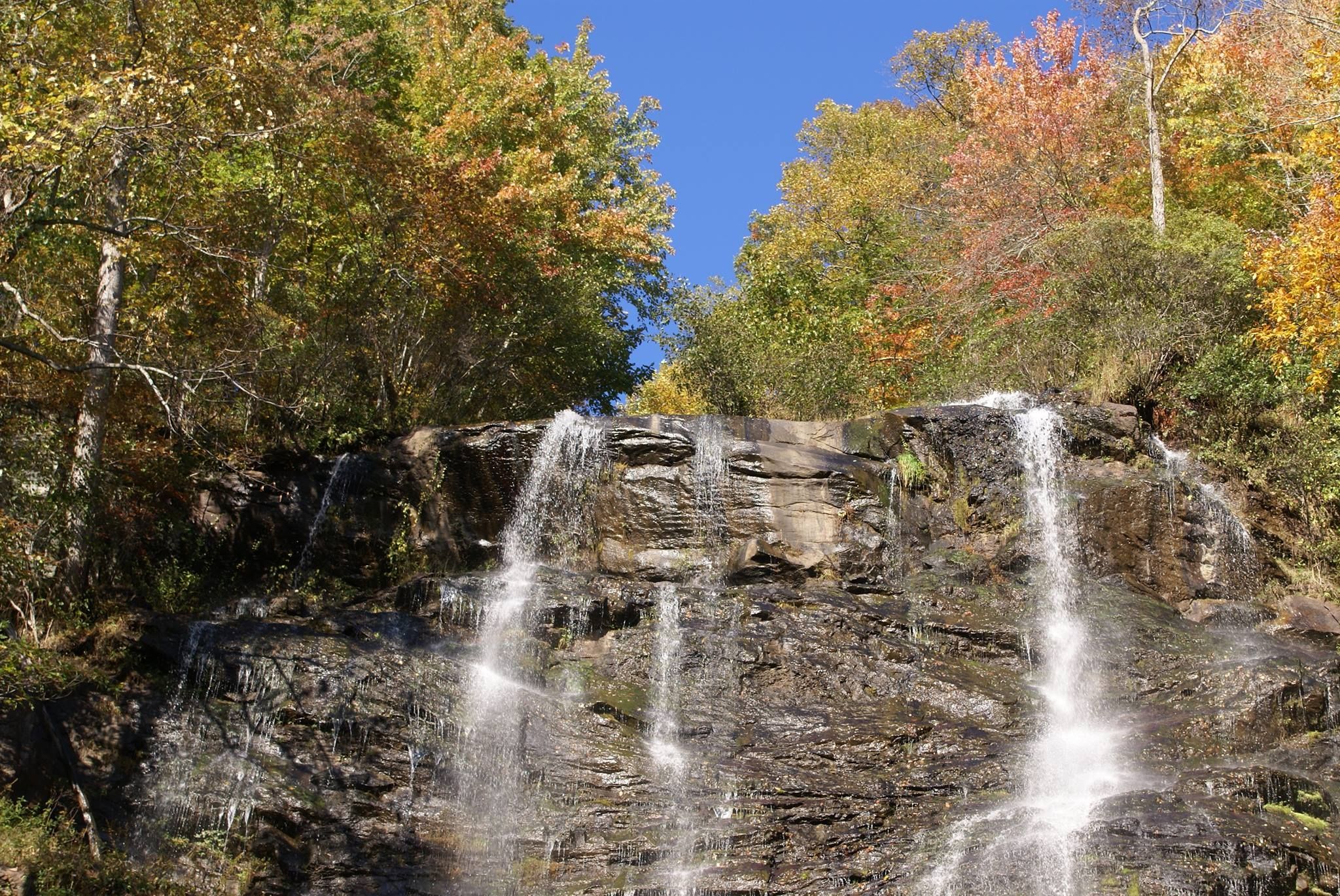 Amicalola Falls cascades down a wide rock face, framed by colorful trees during the fall season. The powerful water flow and open viewing areas make it one of the most photographed waterfalls in Georgia. Visitors often come here for hiking trails, scenic views, and outdoor adventure near the mountains.