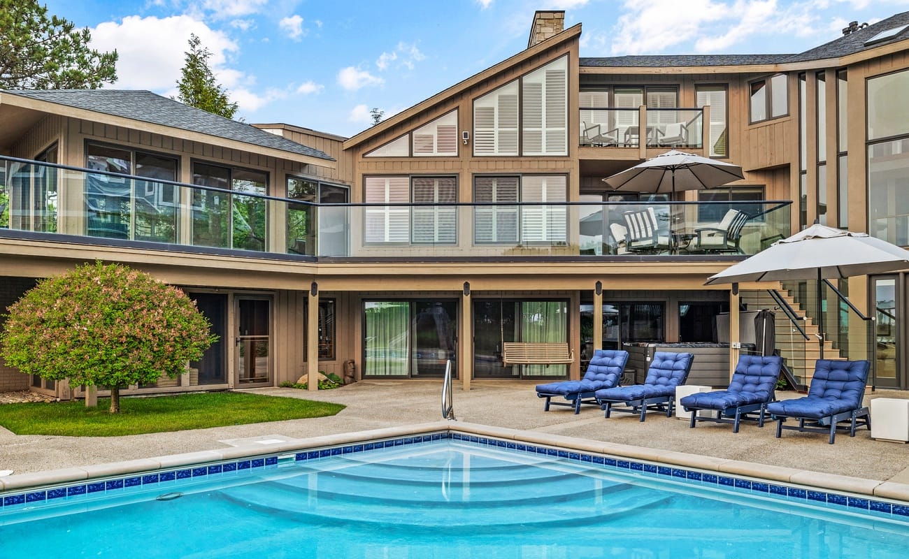 A large backyard pool area with lounge chairs sits behind a modern lake house in Southwest Michigan. The spacious outdoor space is ideal for relaxing, sunbathing, and spending time with family.