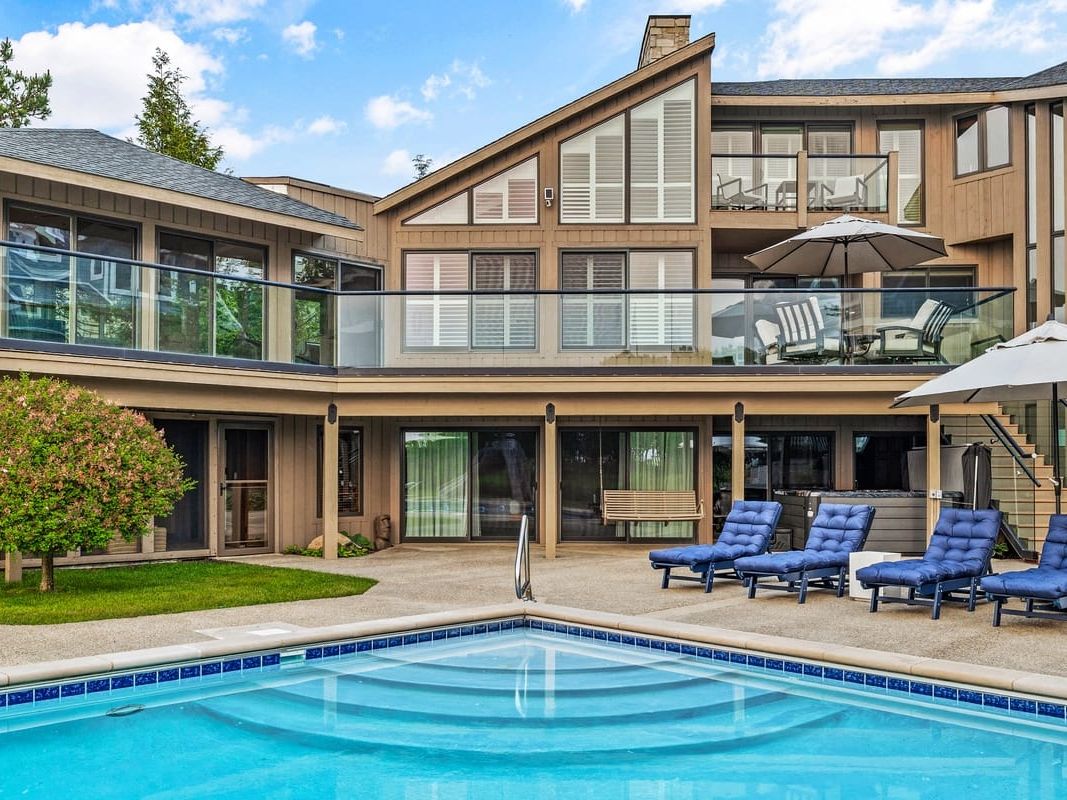A large backyard pool area with lounge chairs sits behind a modern lake house in Southwest Michigan. The spacious outdoor space is ideal for relaxing, sunbathing, and spending time with family.