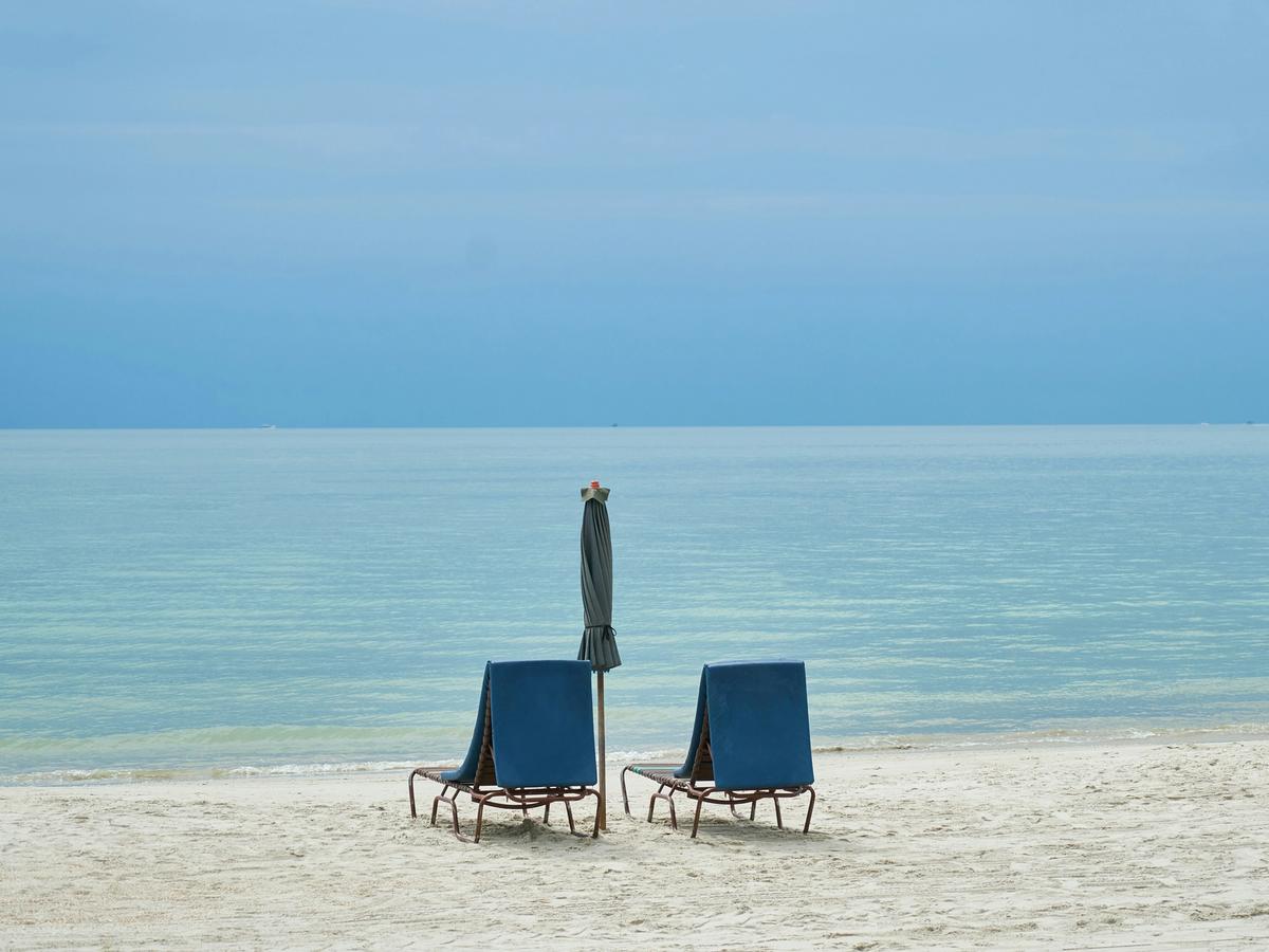Two blue beach chairs with a single umbrella between them and beach ocean views