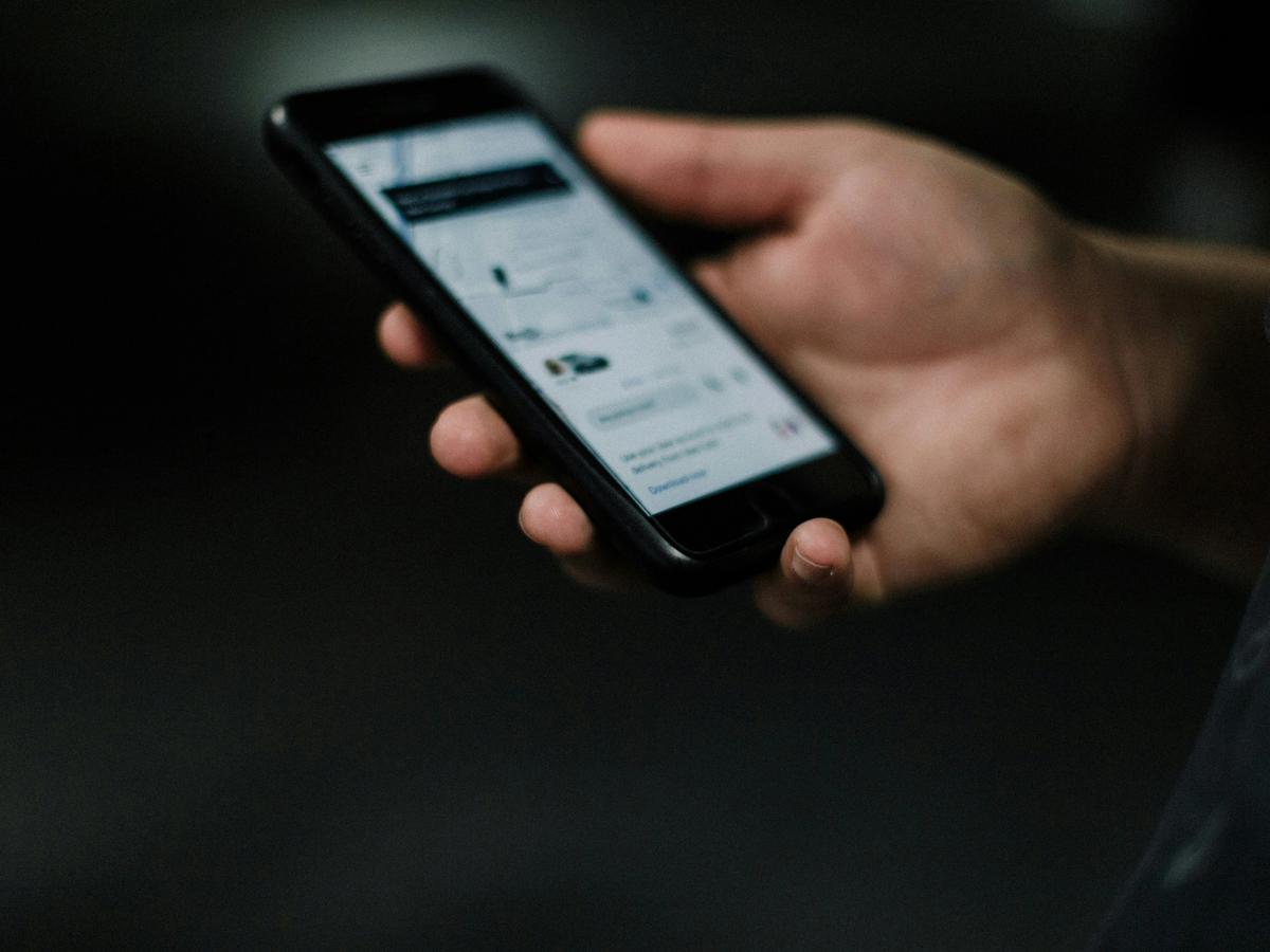 A close-up of a person holding a smartphone, displaying a ride-hailing app interface with vehicle and route details.