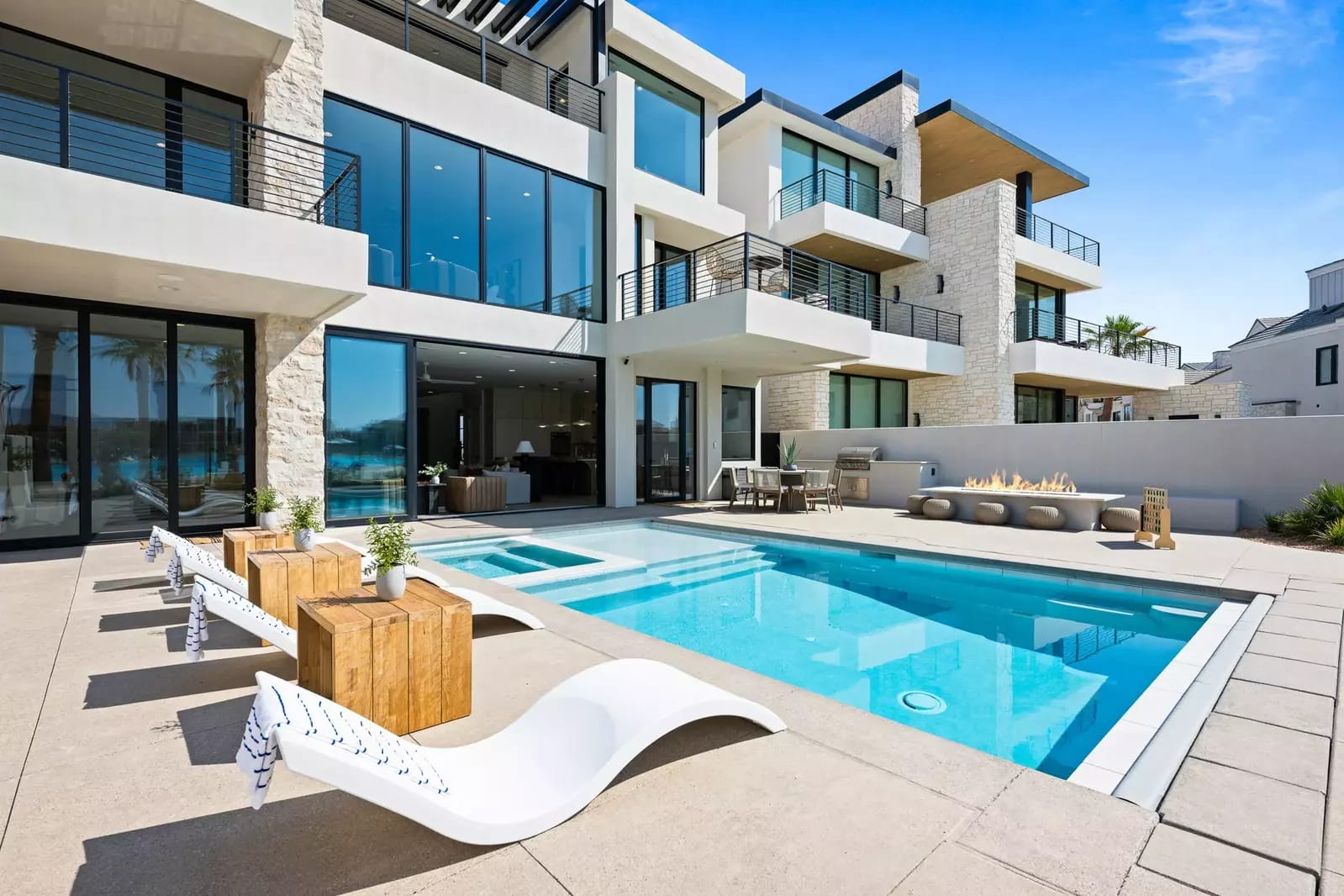 Luxurious modern home with expansive glass walls, multiple balconies, and a private pool with lounge seating and a fire feature.