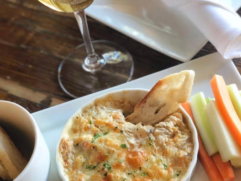 Bread dipped into dip next to celery and carrots and glass of wine