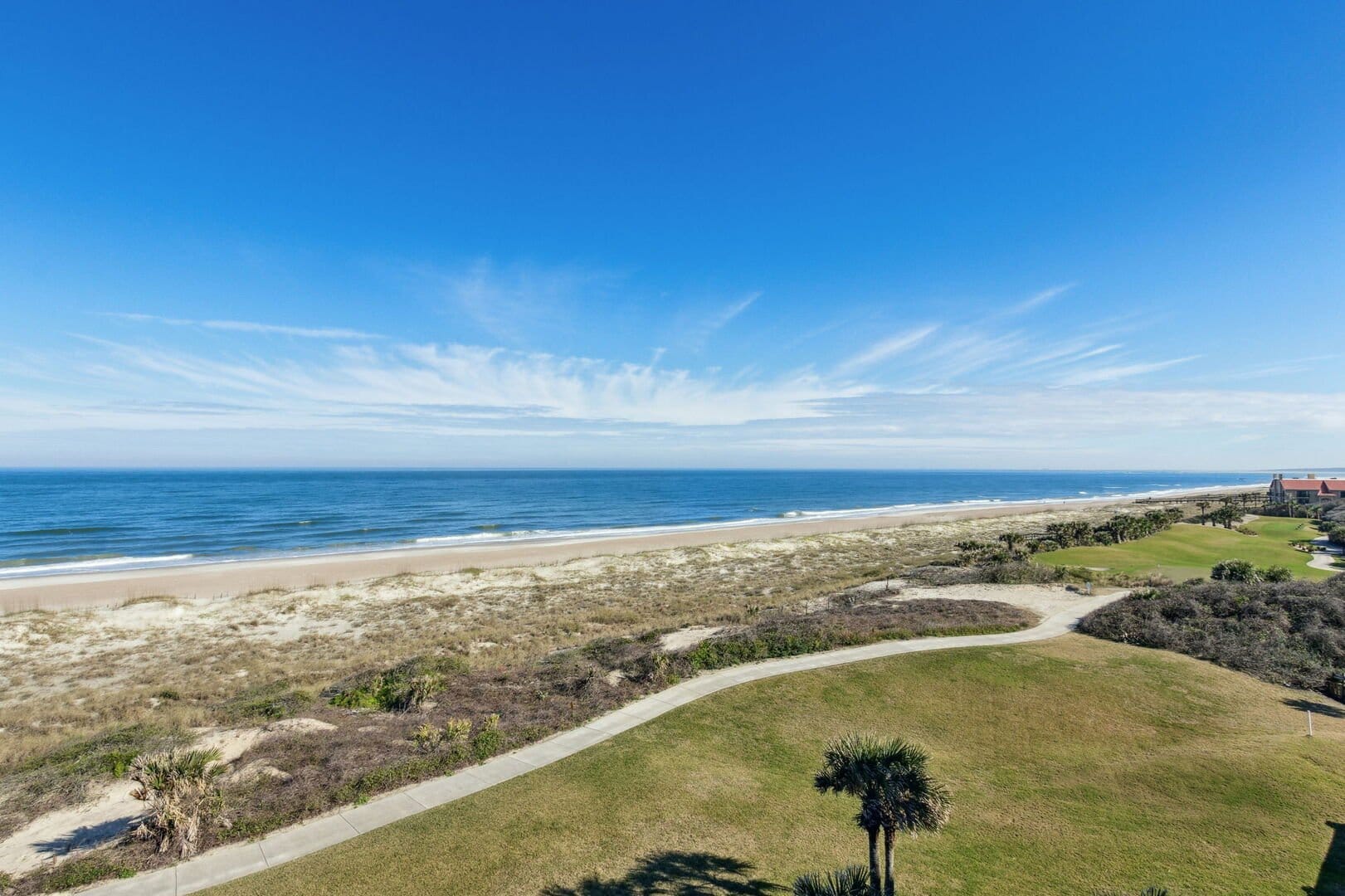 A peaceful view of Amelia Island shows a wide sandy beach, grassy dunes, and a walking path leading toward the ocean. This quiet coastal scene highlights why Amelia Island is known for scenic beach views and calm seaside getaways.
