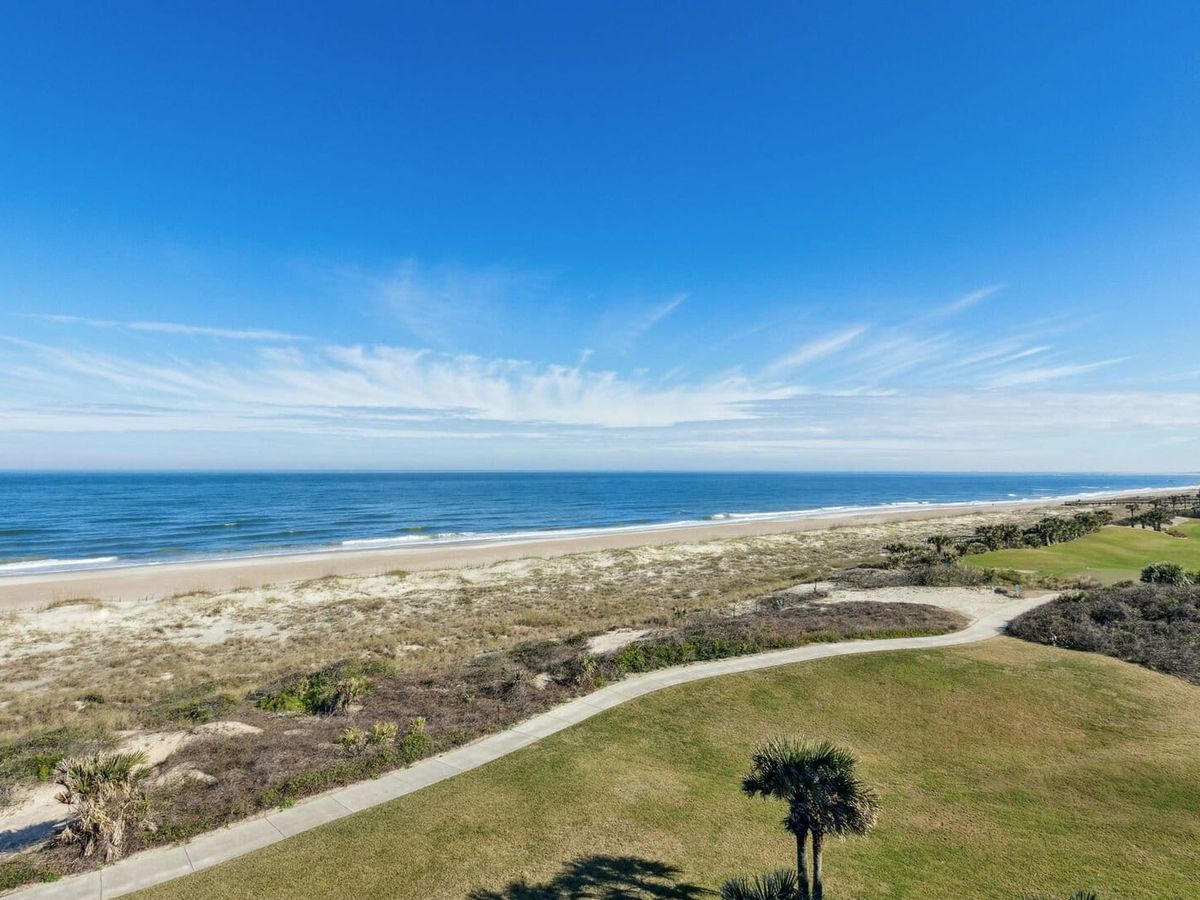 A peaceful view of Amelia Island shows a wide sandy beach, grassy dunes, and a walking path leading toward the ocean. This quiet coastal scene highlights why Amelia Island is known for scenic beach views and calm seaside getaways.