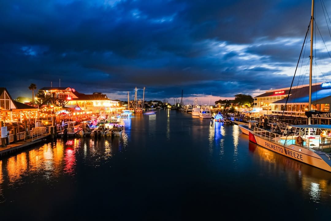 Shem Creek comes alive at night with glowing waterfront restaurants, lively bars, and boats docked along the water. The reflections of lights create a vibrant, welcoming atmosphere perfect for dining and nightlife.