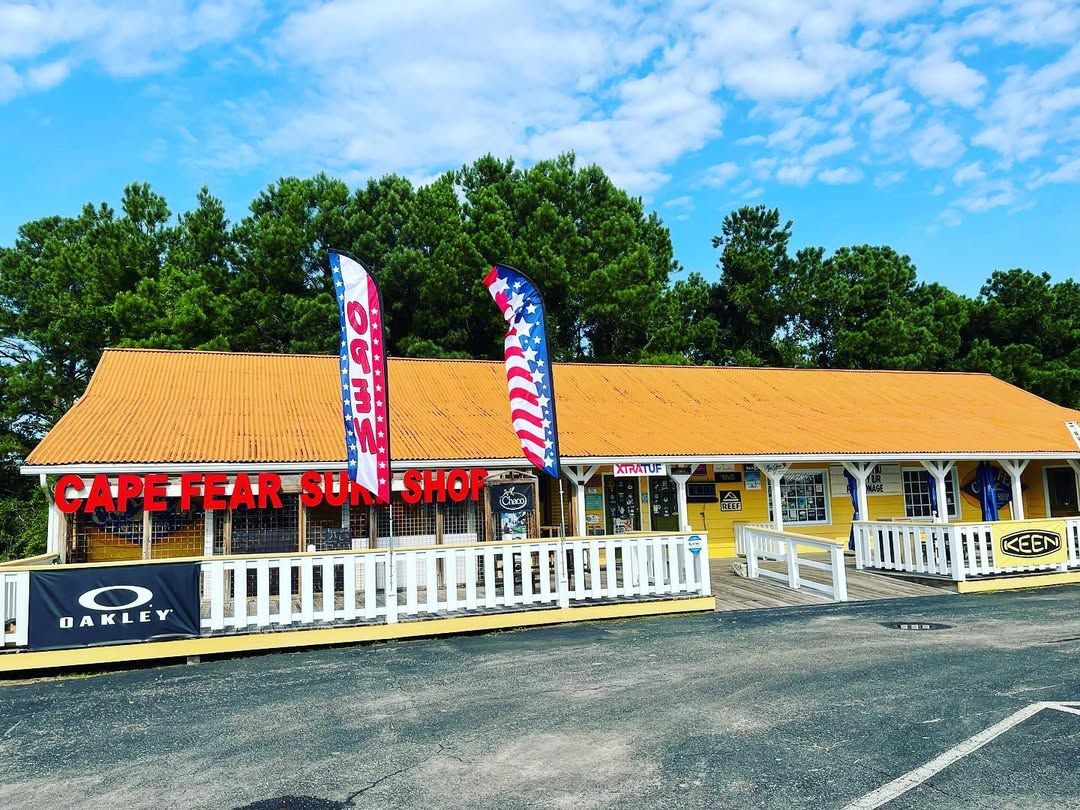 The bright yellow Cape Fear Surf Shop stands out with bold signs, waving flags, and gear for beach days. A fun, local favorite in Holden Beach.
