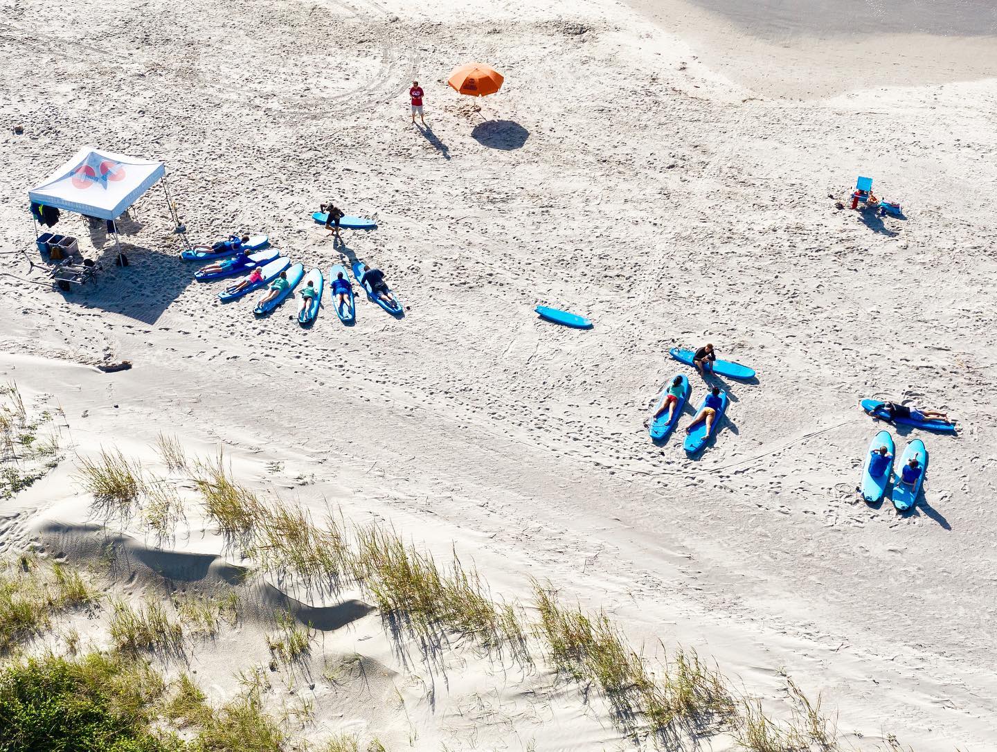 Aerial view of surf students lined up on the sand with blue surfboards during a group lesson at Folly Beach. Instructors guide beginners through the basics before heading into the water. Surf schools like this make learning fun and easy for all ages.