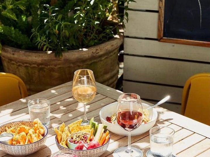 A bright outdoor lunch table filled with fresh veggies, tacos, rosé, and colorful drinks in the sunshine. A cheerful and healthy dining scene.