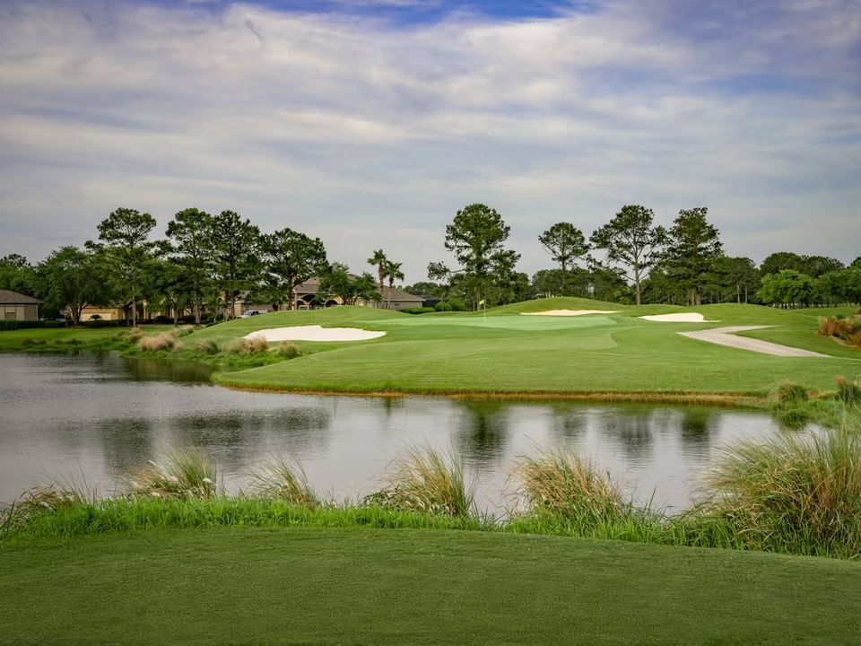 Scenic view of Craft Farms golf course with lush greens, a pond, and palm trees. Ideal for a relaxed round of golf during your beach vacation.