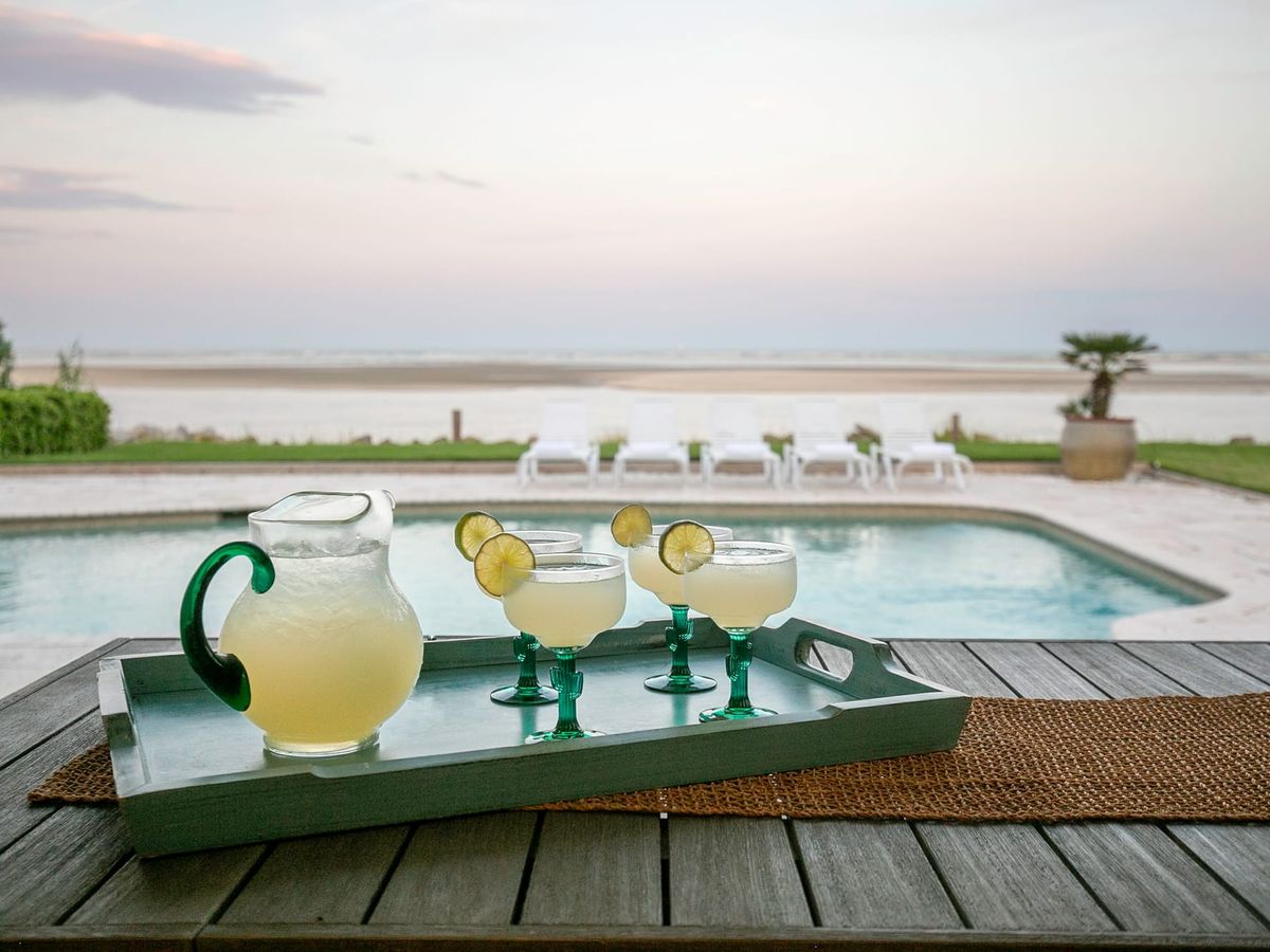 margarita pitcher and glasses with lime wheels in them with private pool in front of them